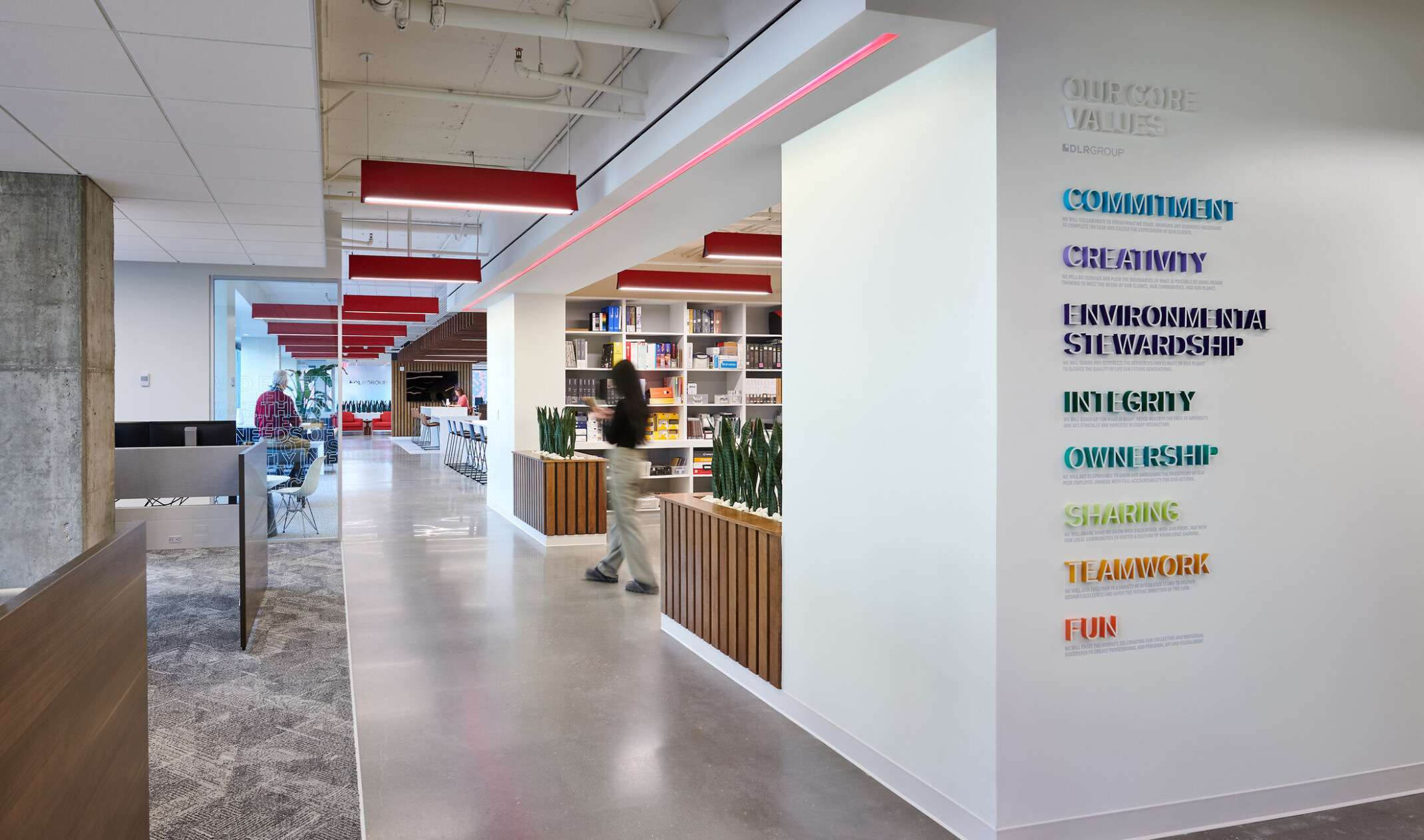 modern workplace with values displayed on the foreground wall in rainbow colors, acoustic panels hang from ceiling, long hallway with wood wane scotting