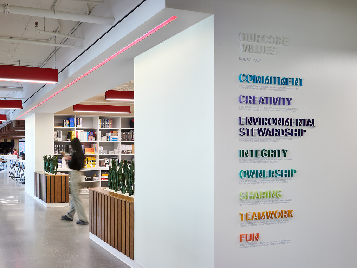 modern workplace with values displayed on the foreground wall in rainbow colors, acoustic panels hang from ceiling, long hallway with wood wane scotting