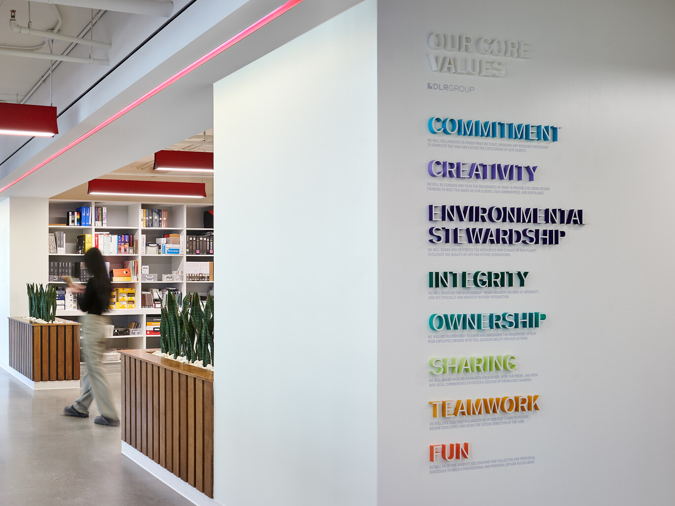 modern workplace with values displayed on the foreground wall in rainbow colors, acoustic panels hang from ceiling, long hallway with wood wane scotting