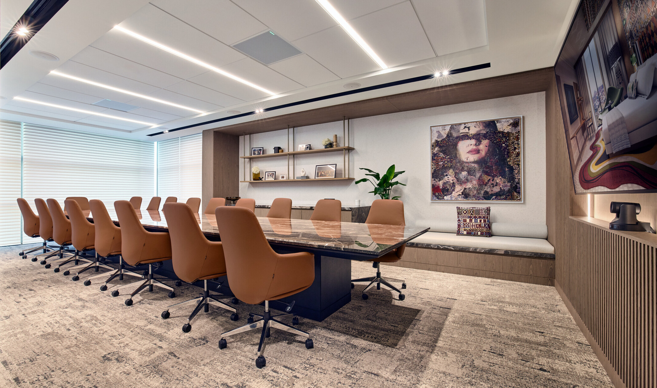 A sleek, modern conference room featuring a long marble table surrounded by tan leather swivel chairs. The space is accentuated by contemporary artwork, soft lighting, and neutral tones.