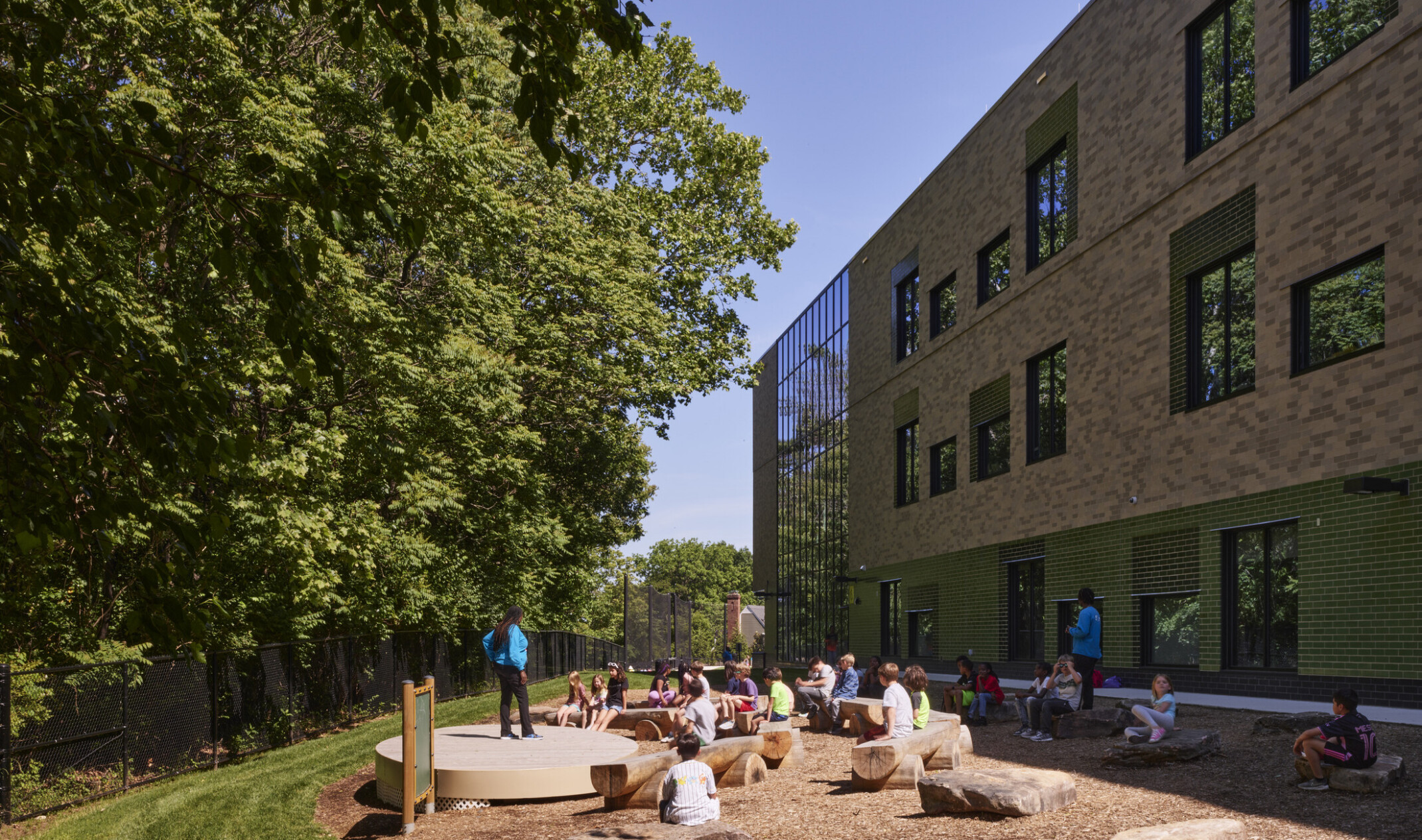 Outdoor learning area next to a multistory school filled with rocks and cut log seating looking at a densely wooded area