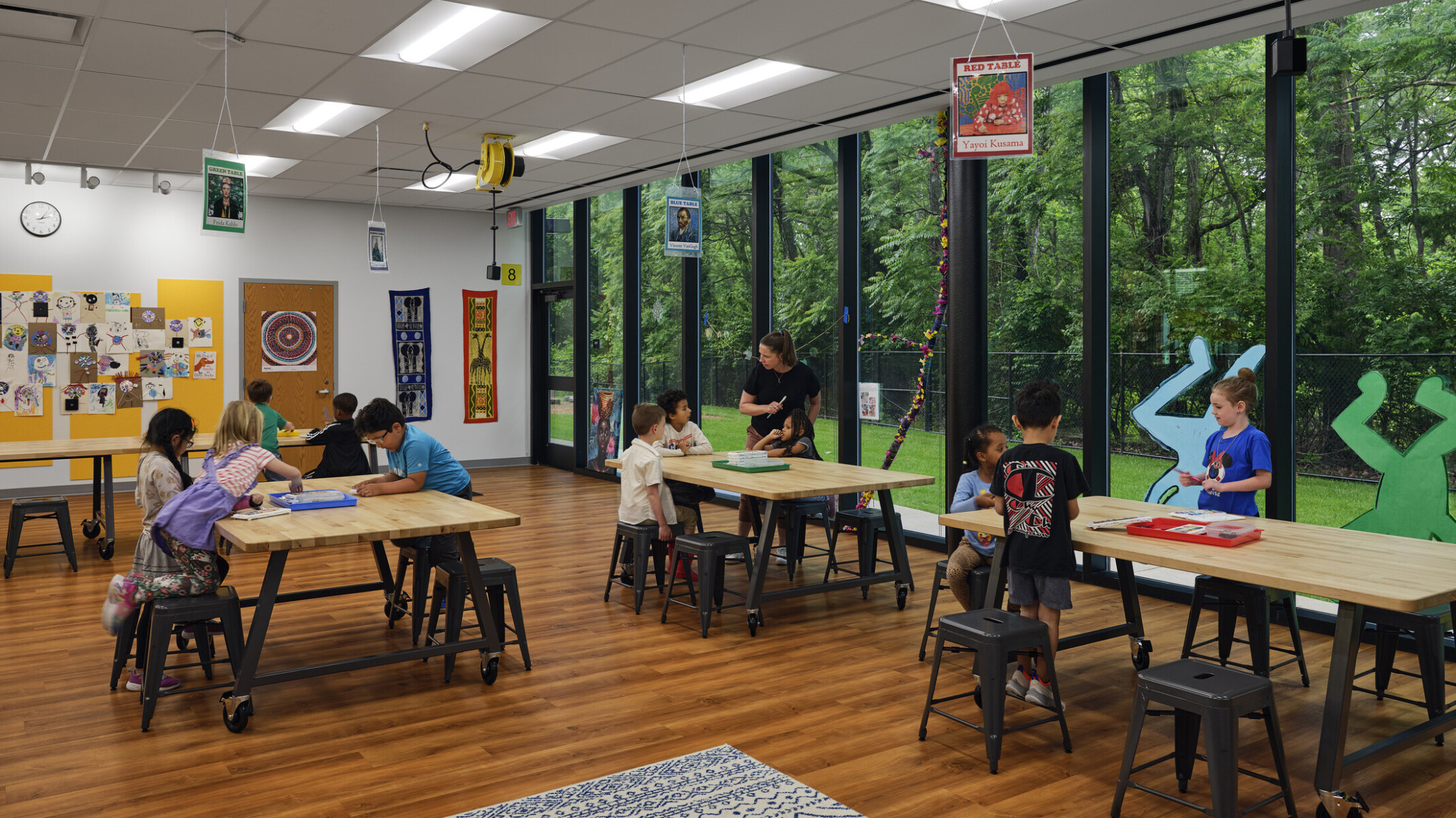 Elementary school classroom filled with tables and chairs with a large wall of windows