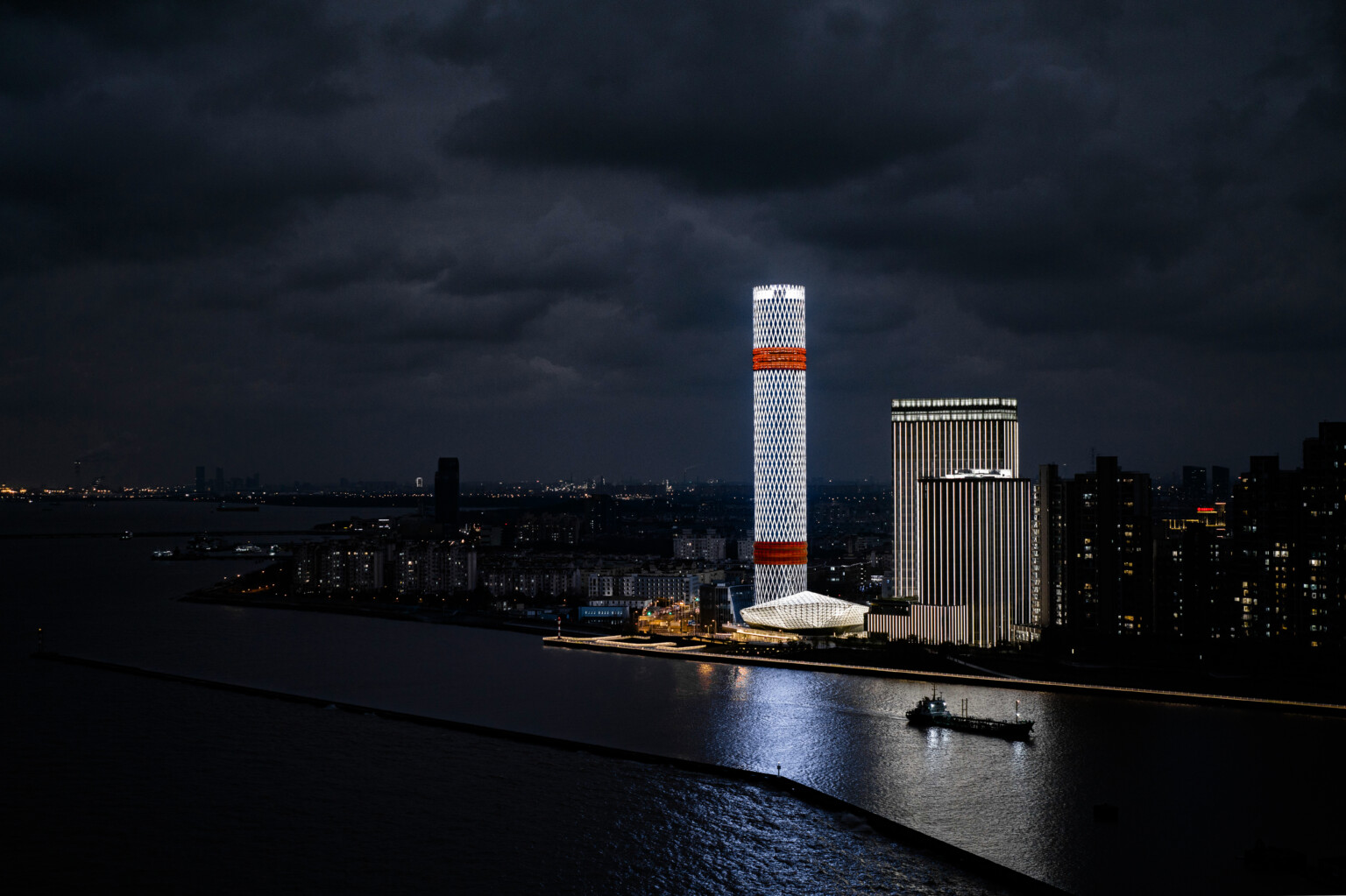 Baoshan Long Beach Complex illuminated at night along Shanghai's Yangtze River, diamond geometric light on cylindrical tower