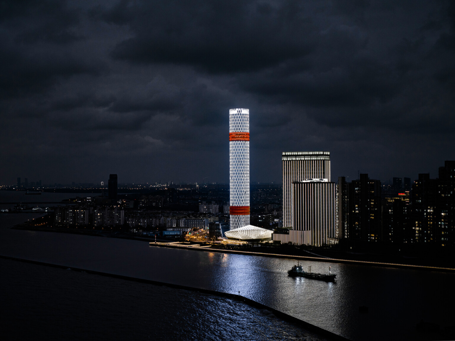 Baoshan Long Beach Complex illuminated at night along Shanghai's Yangtze River, diamond geometric light on cylindrical tower