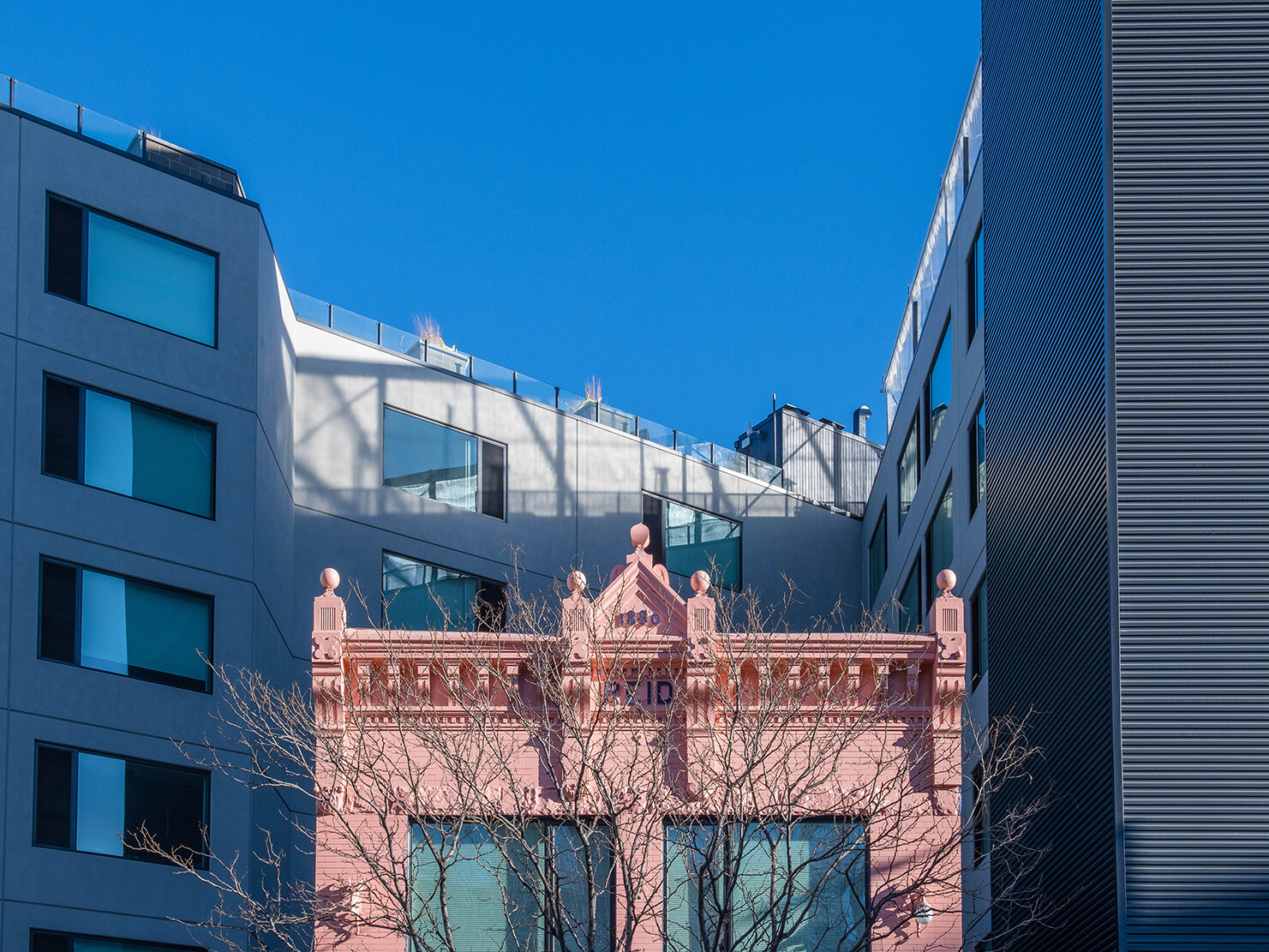 pink neoclassical brick facade with large glass windows nestabled between blue and green modern steel and glass buildings pink neoclassical brick facade with large glass windows nestabled between blue and green modern steel and glass buildings