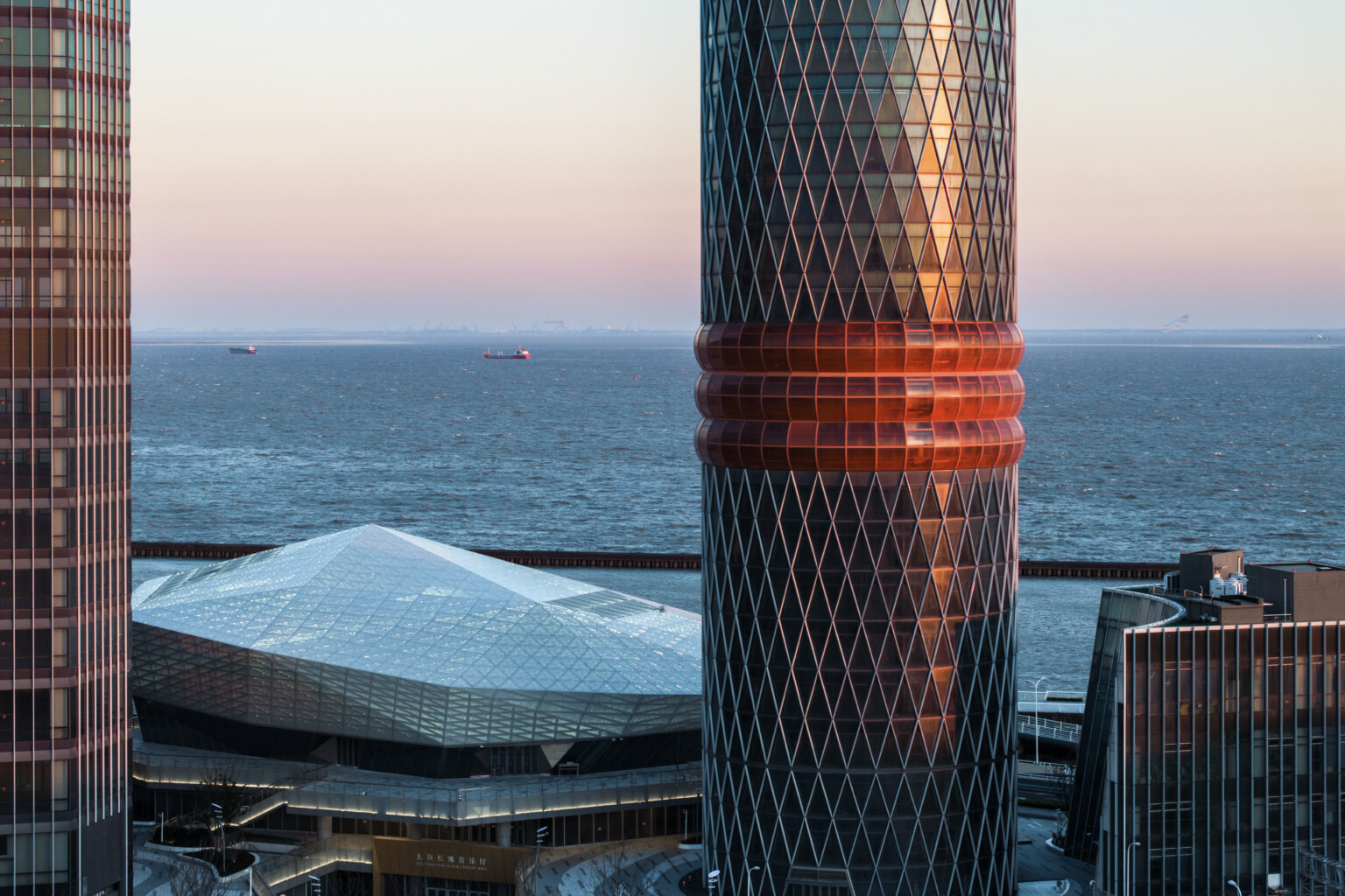 side view of tower with three red bands, view of diamond shaped angular arts building and river beyond