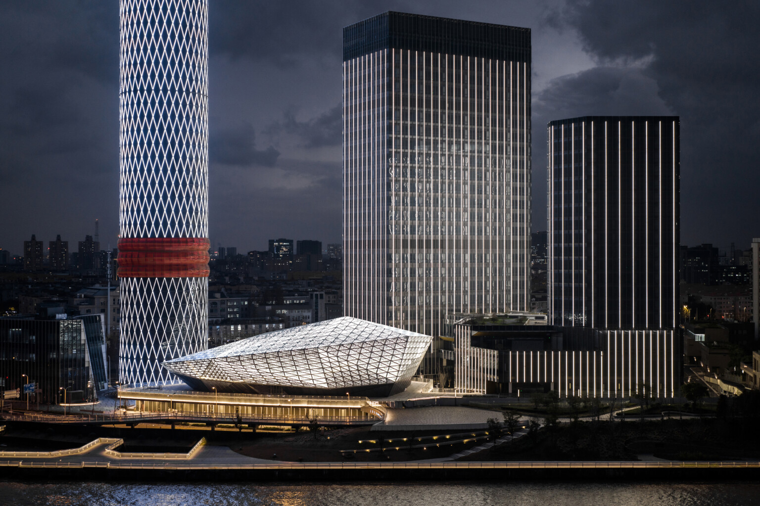 View from rier of illuminated complex at night, angular diamond shaped building lit from within through triangular panels