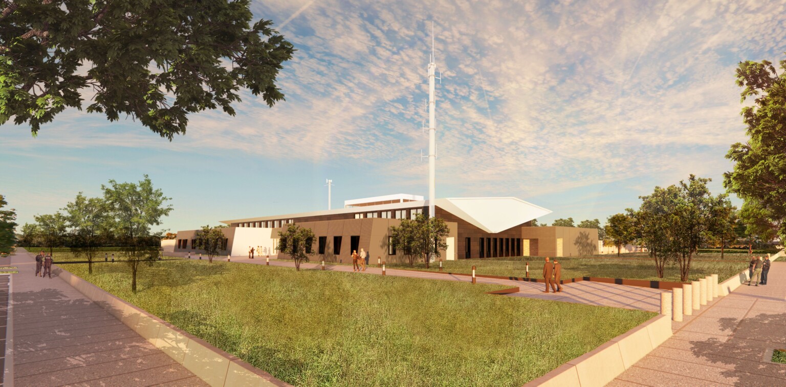 Rendering of Lake County Regional Operations & Communications Facility; one-story brick building with white butterfly wing roof and tall communications antenna on a grassy site with wide sidewalks around the perimeter and a main drive that is protected by bollards at the entrance