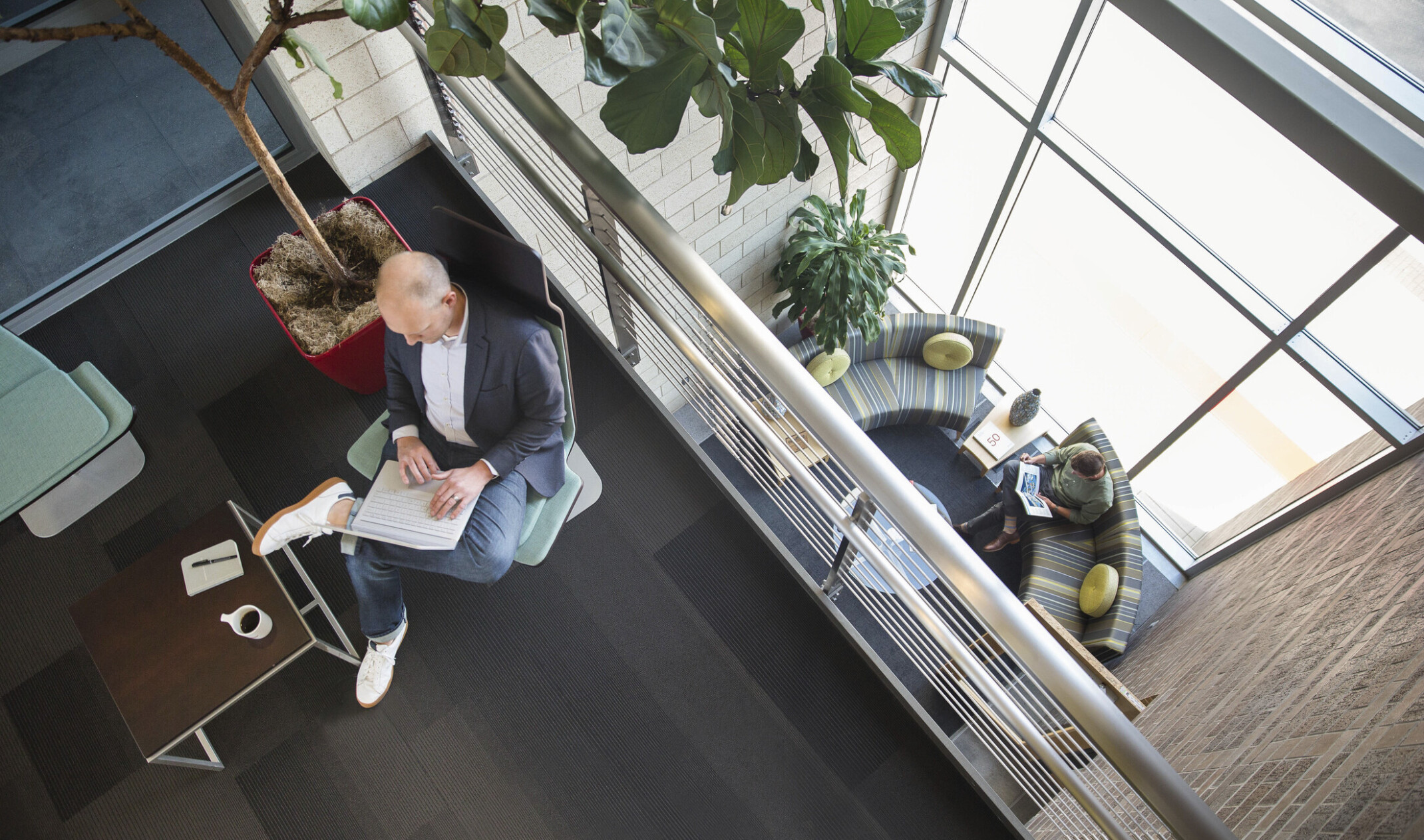 interior balcony looking down to couches by double height windows. Potted plants on both levels