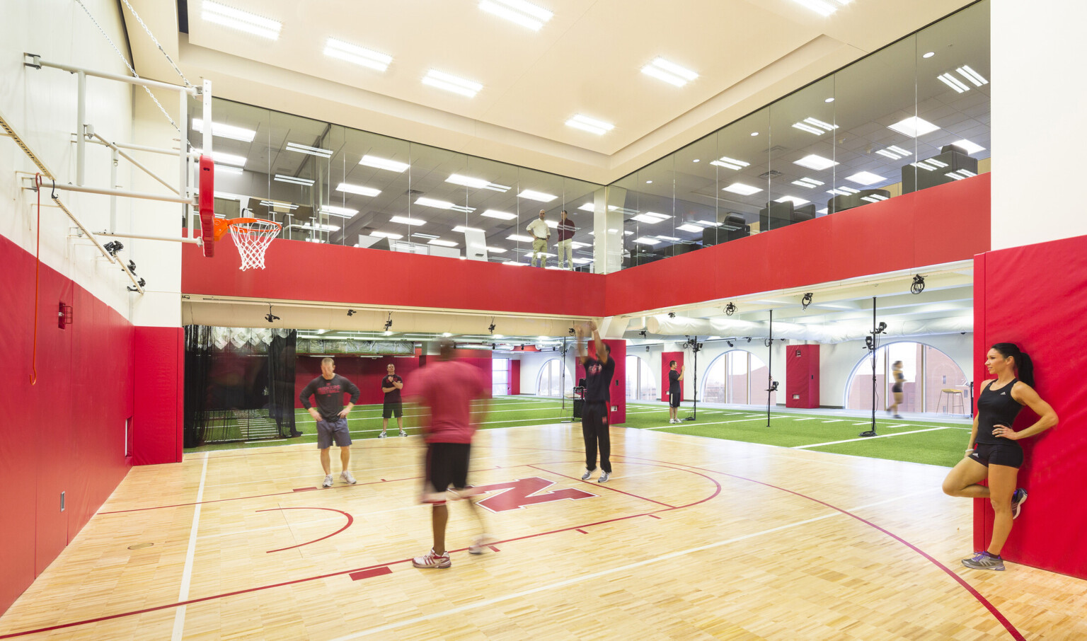 Double height basketball half court with floor to ceiling windows on 2nd floor. Turf floor on sides, arched windows to right