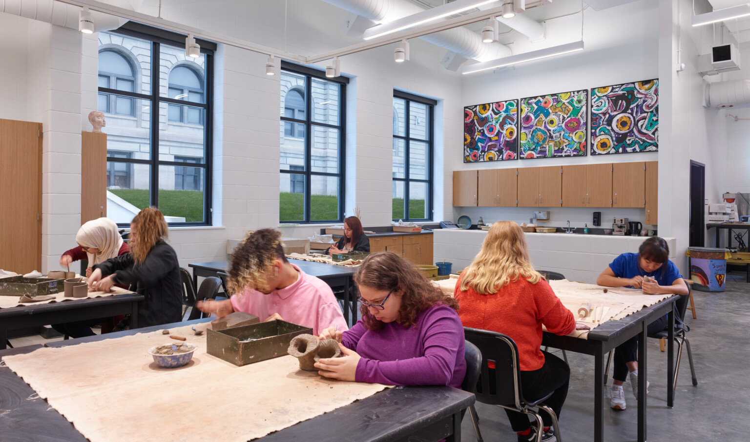 students working on ceramics in a modern art classroom; large art mural covers the back wall, restored historic windows bring in light