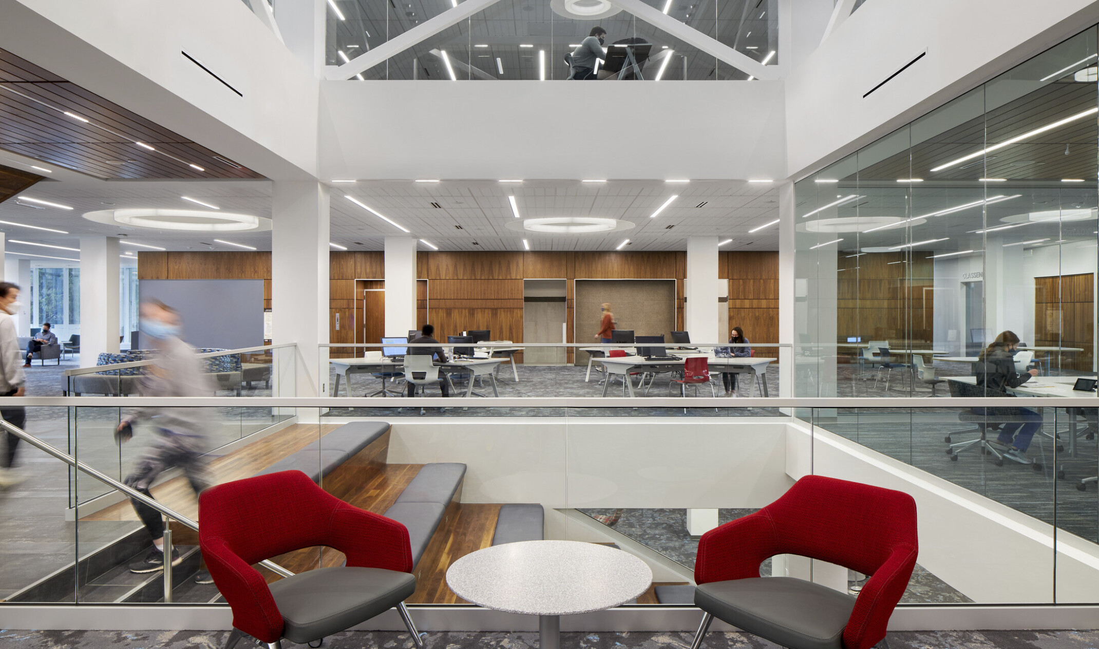 Two red seats in large atrium area with stairs down to lower level, white walls, wood paneling, and grey carpet
