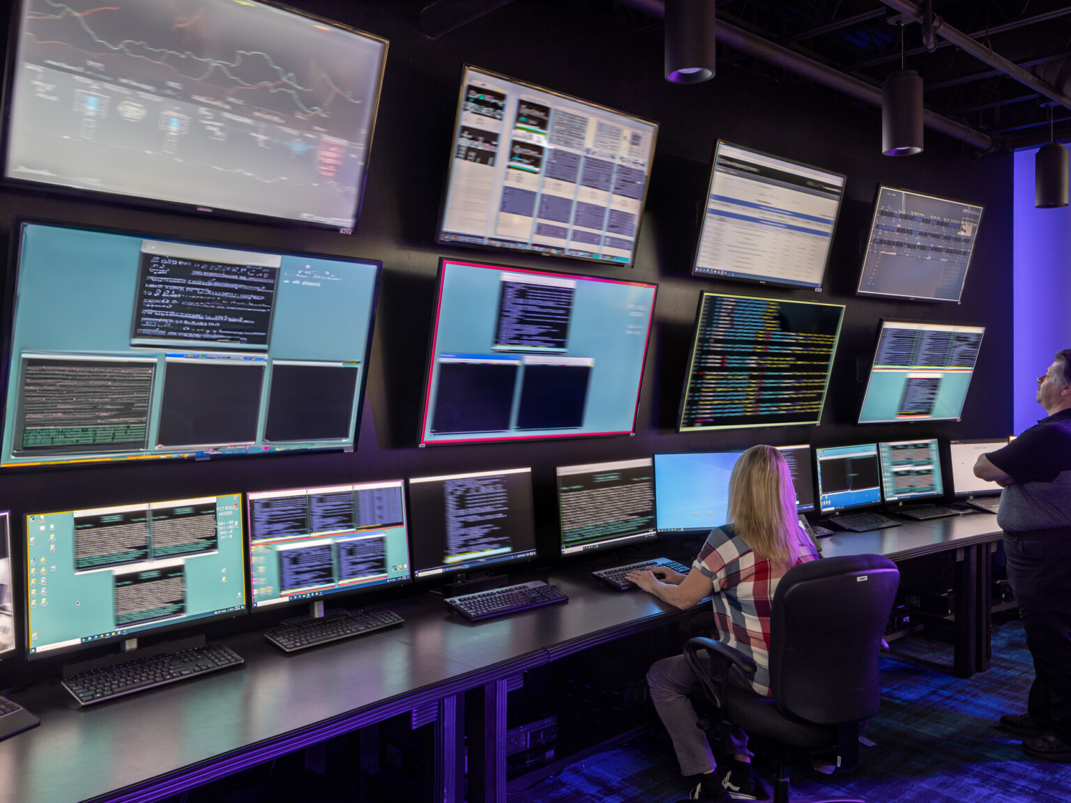 technician monitors wall of large display screens show data of server farm to ensure server uptime and stability
