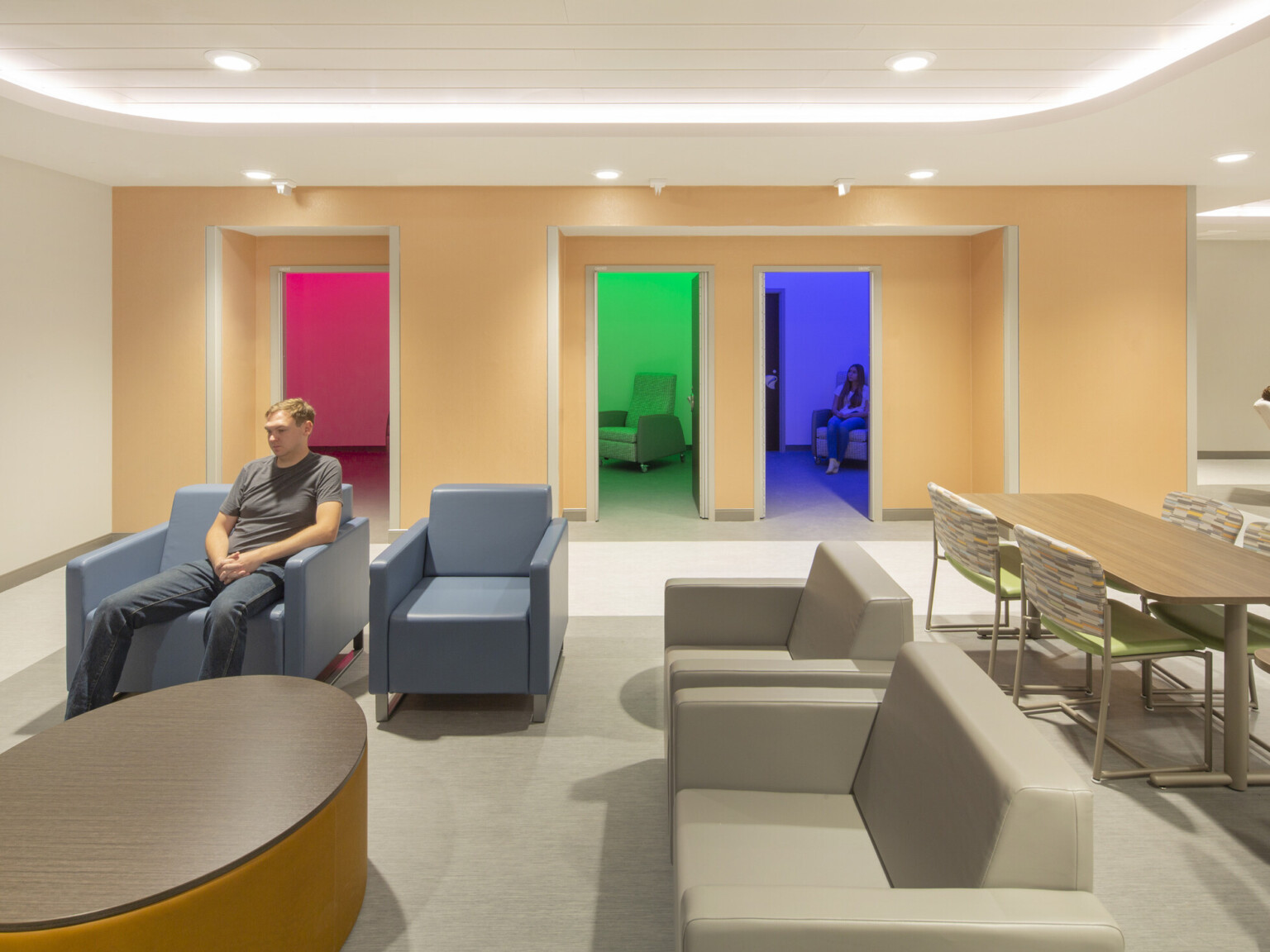 Seating area in front of small recessed rooms with red, green, or blue light. Arm chairs in each room and outside