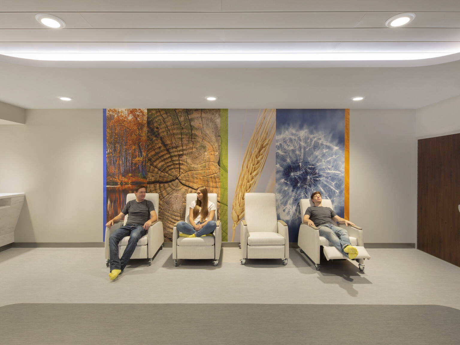 Nebraska Medicine Psychiatric Emergency Services Unit interior hallway, three people sit in recliners in front of photo mural