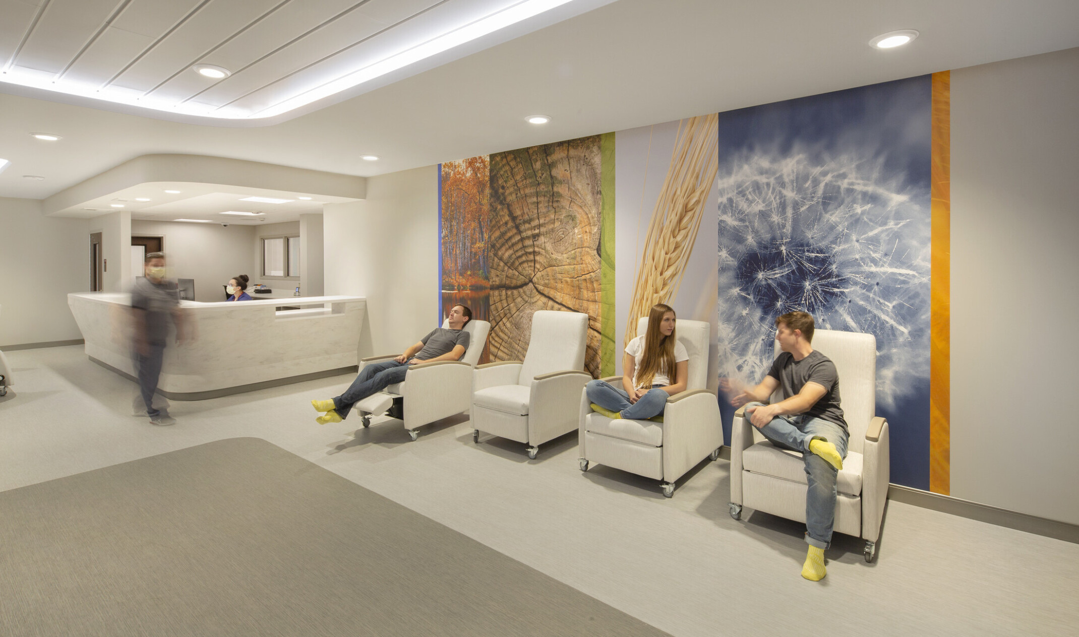 Nebraska Medicine Psychiatric Emergency Services Unit interior hallway. 3 people sit in recliners in front of photo mural