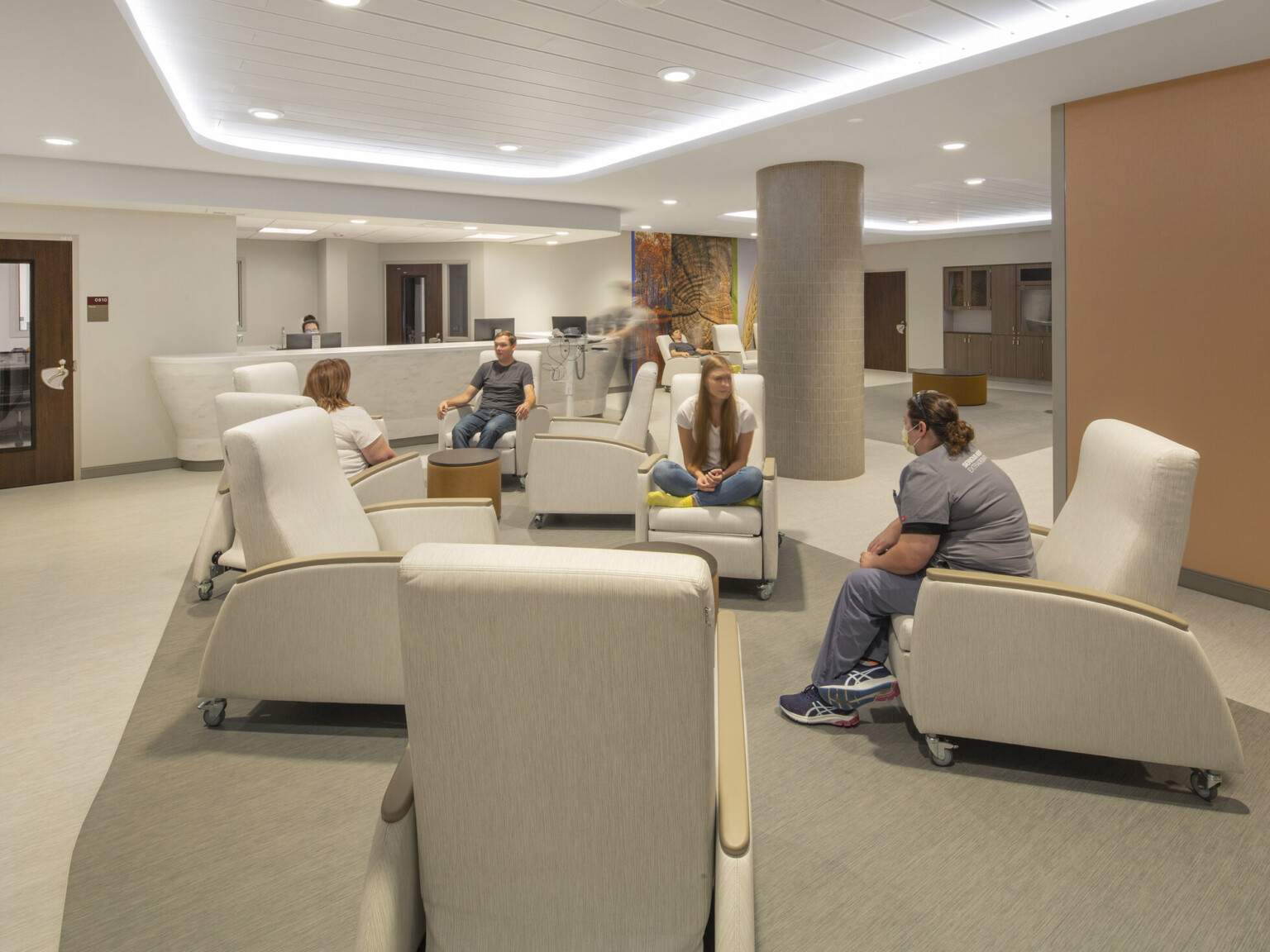 People in wheeled arm chairs in groups around round tables in big room with illuminated recessed ceiling detail, orange wall