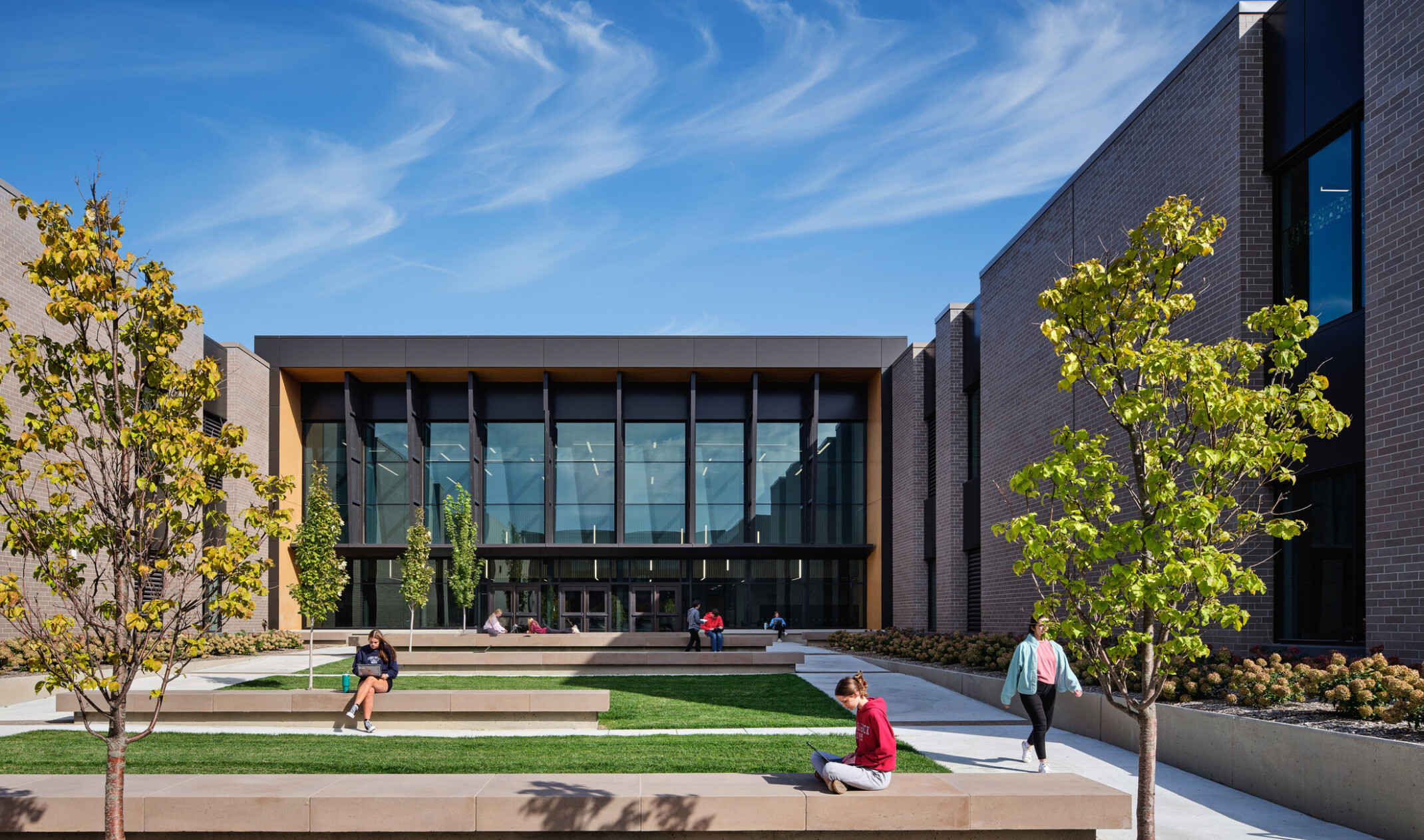 Courtyard with lush green landscaping surrounded on three sides by a multilevel tan brick school building with dark brown accents