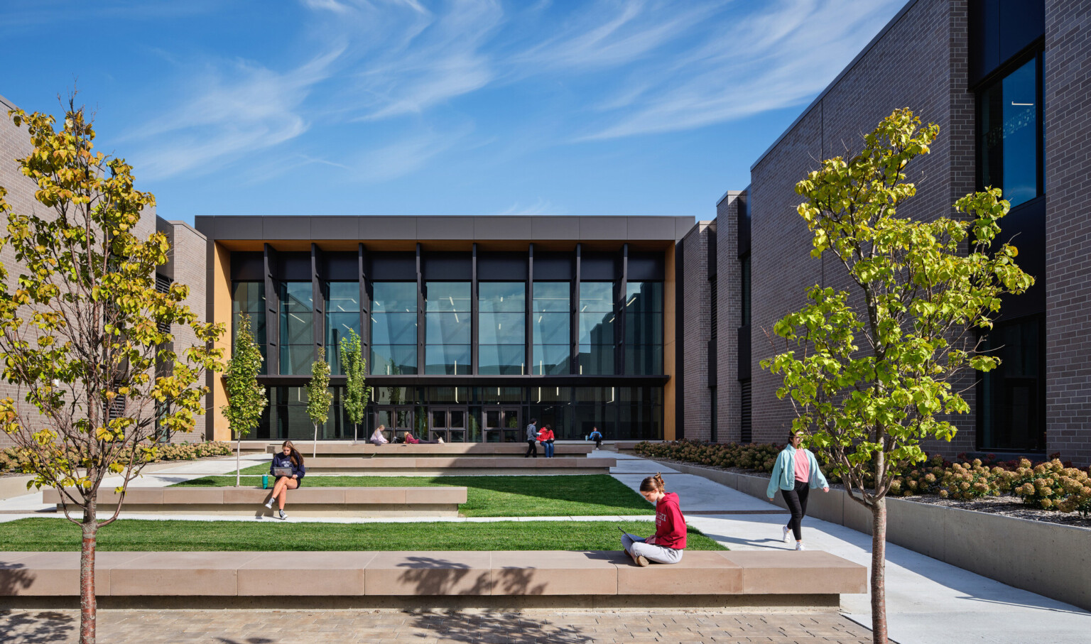Courtyard with lush green landscaping surrounded on three sides by a multilevel tan brick school building with dark brown accents Courtyard with lush green landscaping surrounded on three sides by a multilevel tan brick school building with dark brown accents