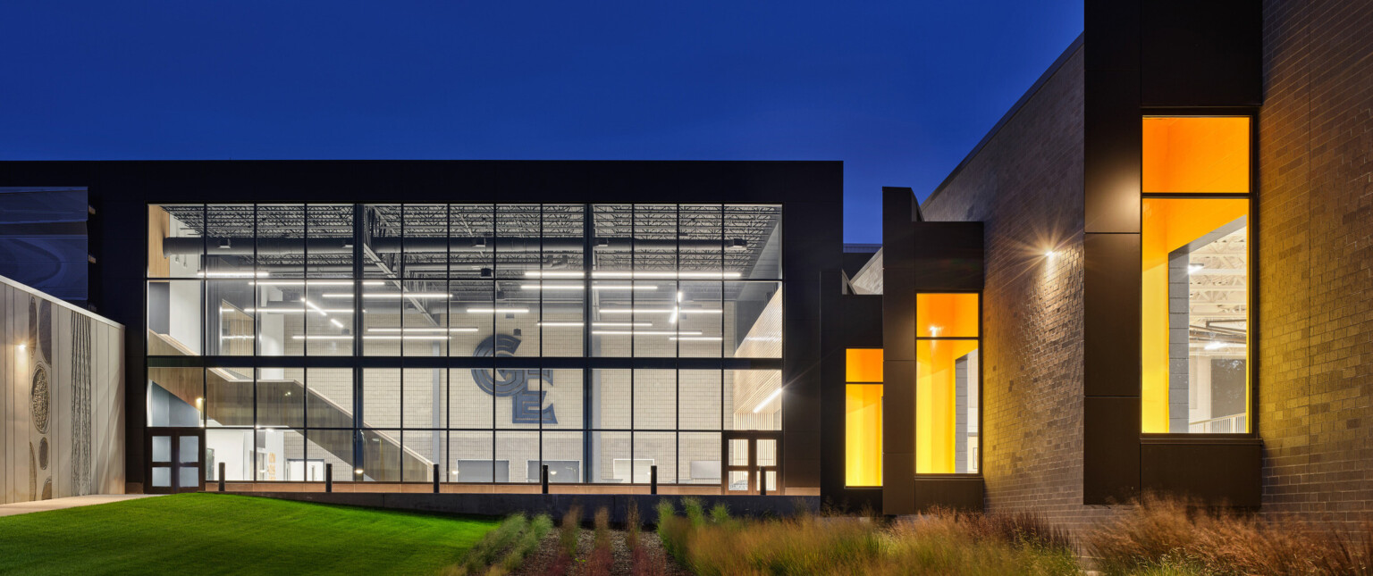 Night image of a tan brick building surrounding a courtyard with large windows filled with light