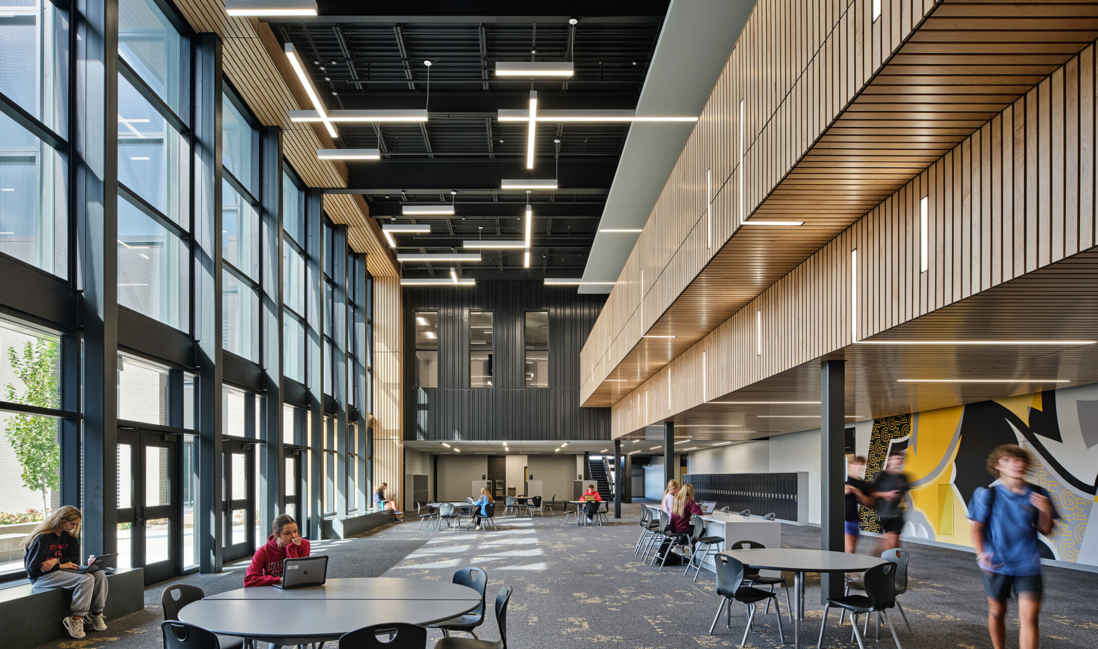 Long hallway filled with tables and chairs with a second story overlooking with large windows