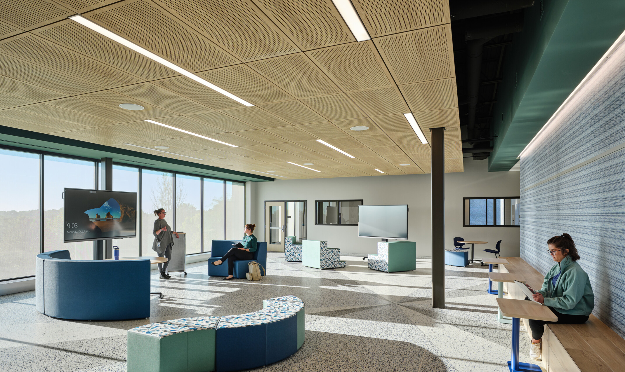 A gathering area at Boys Town Education Center with modern blue and green seating with light wood ceiling, wall of windows, and a colorful accent wall for trauma informed design