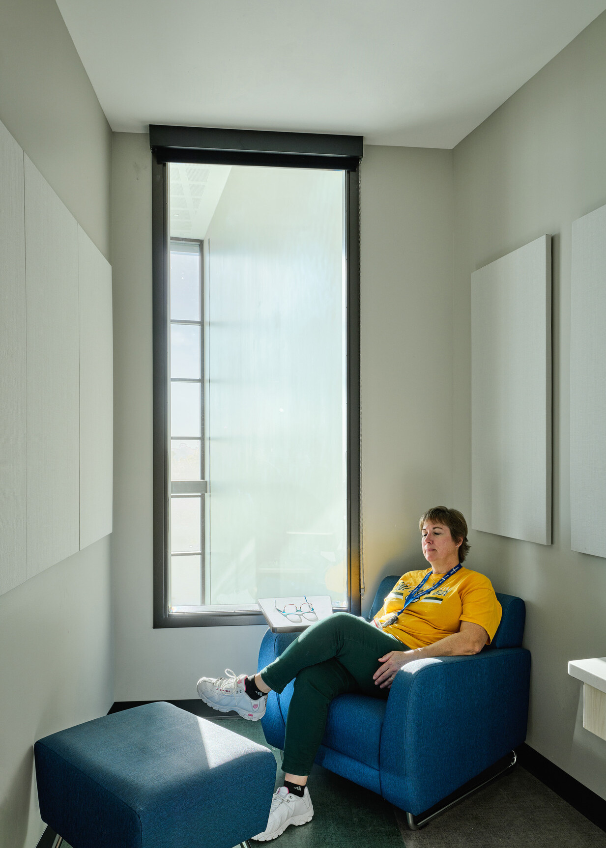relaxation room in Boys Town Education Center; woman in a yellow shirt sitting in the corner comfy chair in a small closet like room with a large window behind her; room for trauma informed design