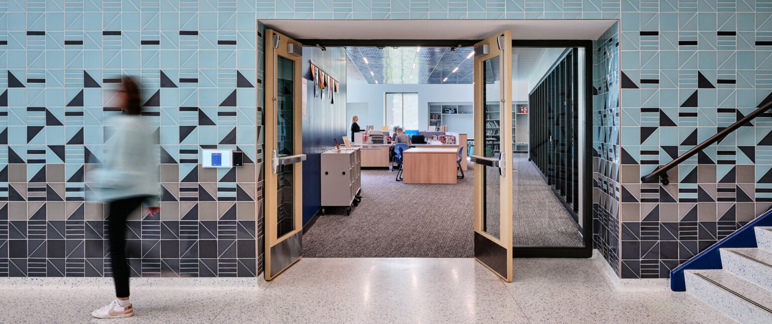 Abstract blue and grey tile wall surrounding a door opening looking into a office with light wood furniture