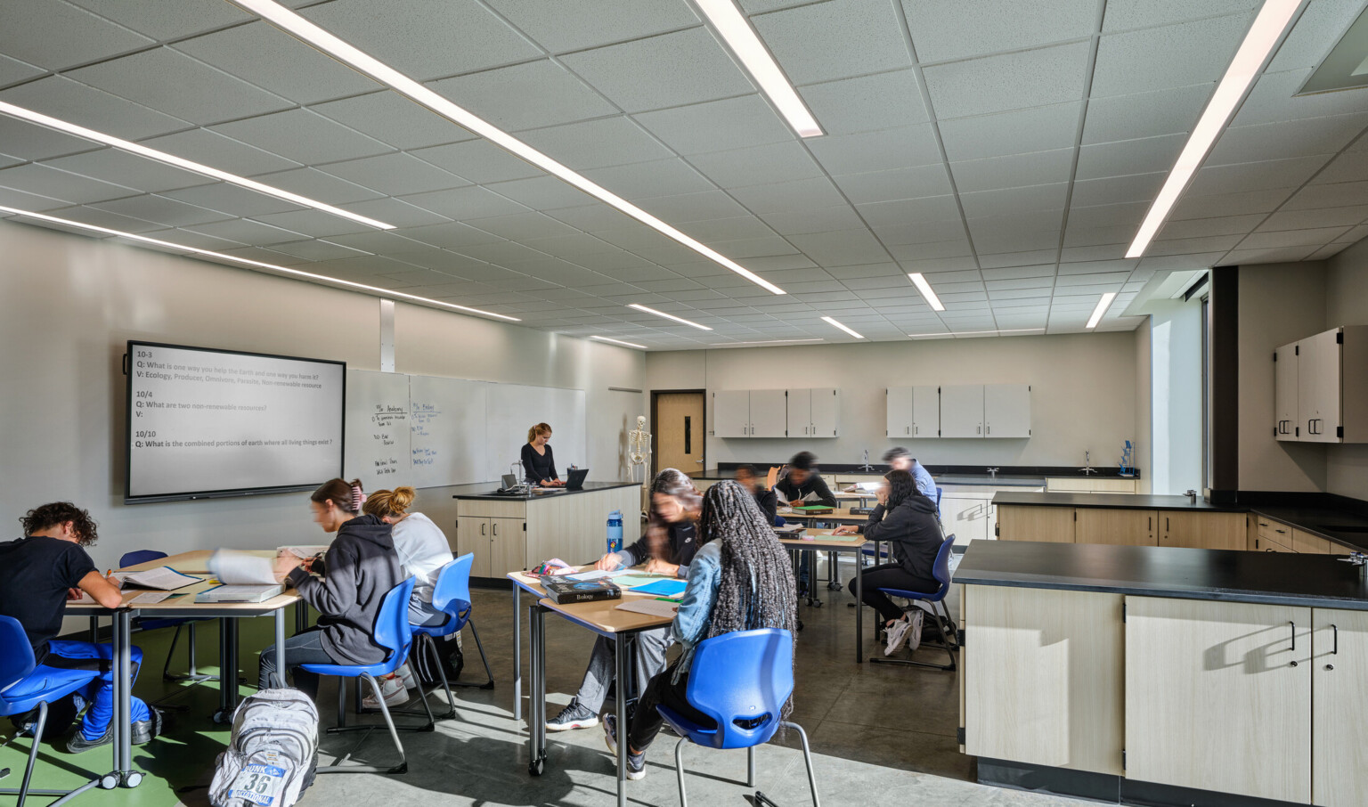 students in a classroom at Boys Town Education center; pod desks with 2-4 students at each; lab-style counters with whiteboard and tech screen at the front of the classroom; minimal distraction for trauma informed design