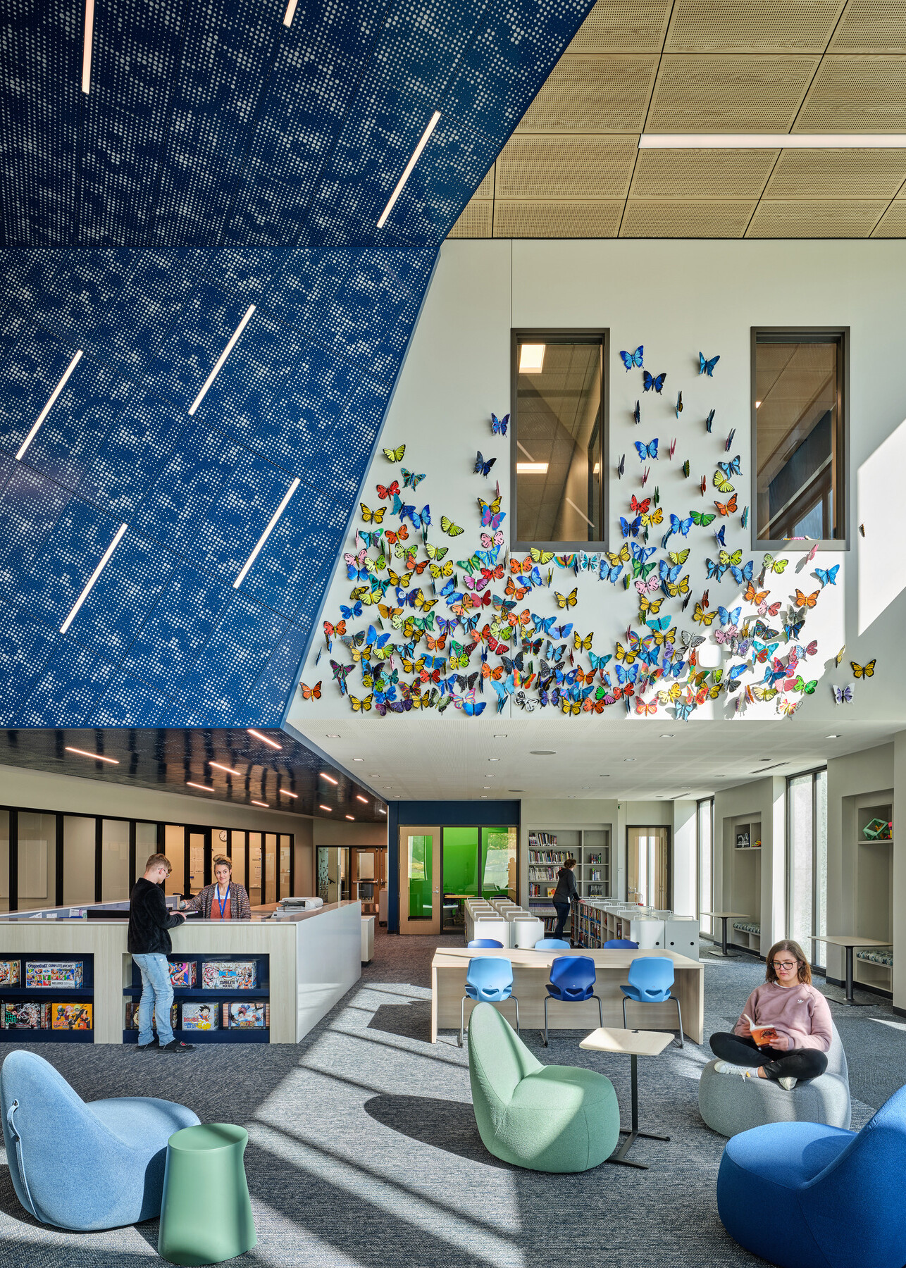 double height space in Boys Town Education Center; upper wall Mural wall with dimensional butterflies, blue textured wall, interior windows; varied seating for students and teachers; trauma informed design