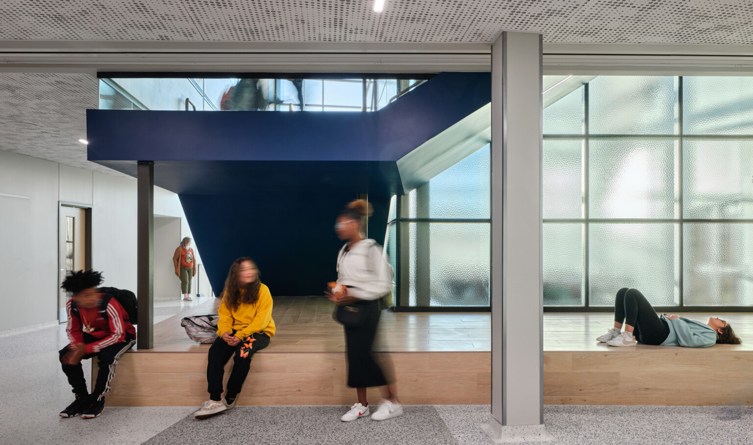 Kids gathered in a school common area with a light wood raised seating area and a blue staircase
