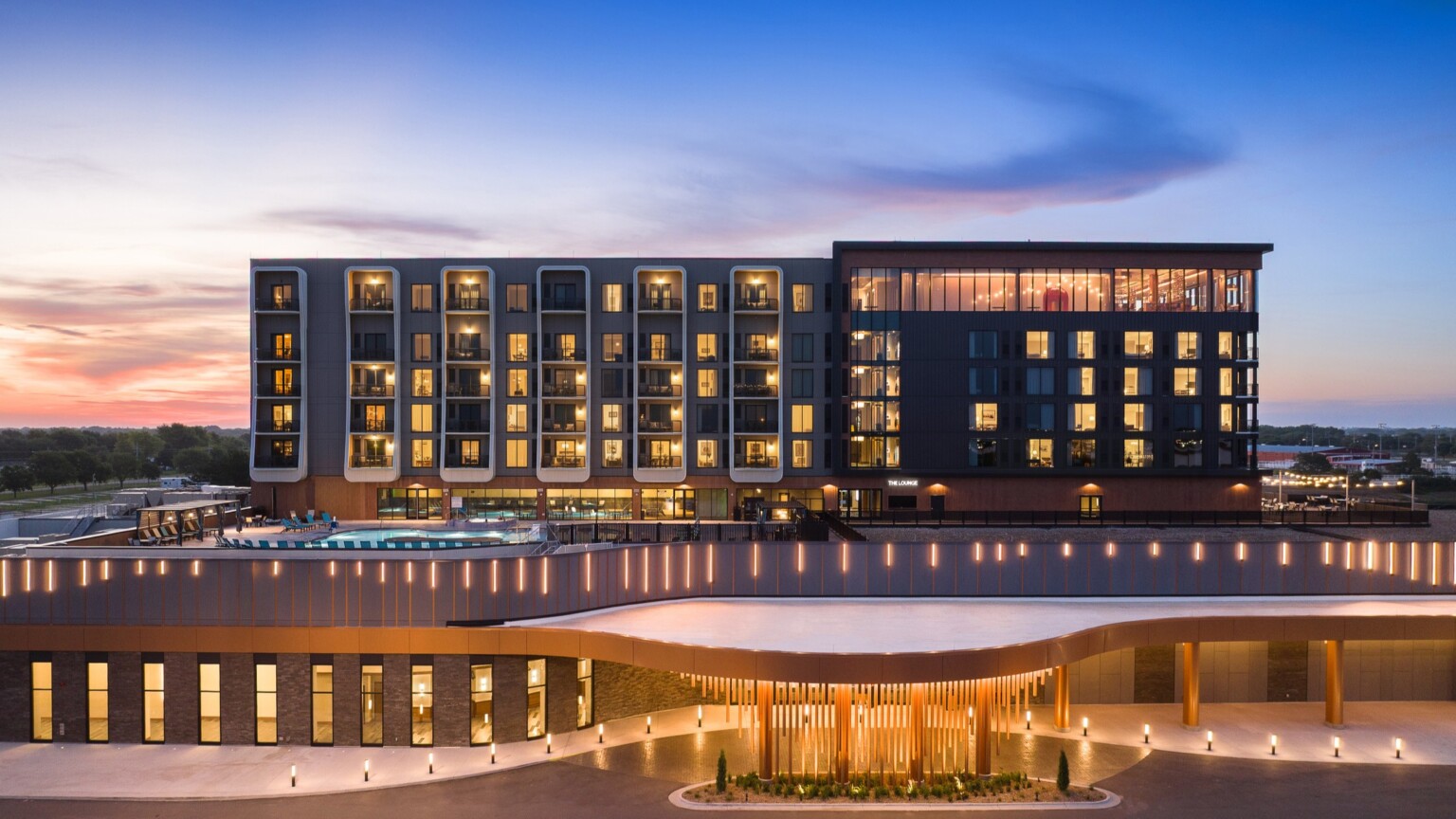 modern tower Resort building and pool deck illuminated at dusk, with entrance in view; front entrance image of Grand Island Casino Resort at Fonner Park