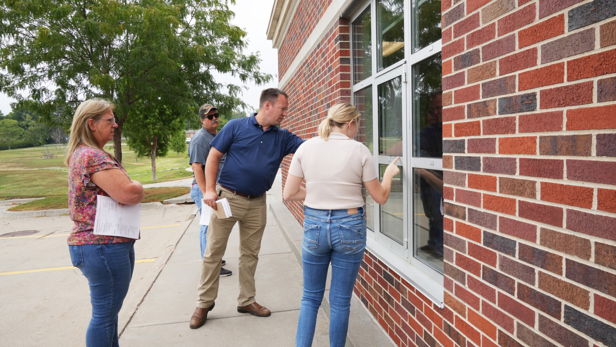 Four individuals inspect a window on a building with a red brick façade