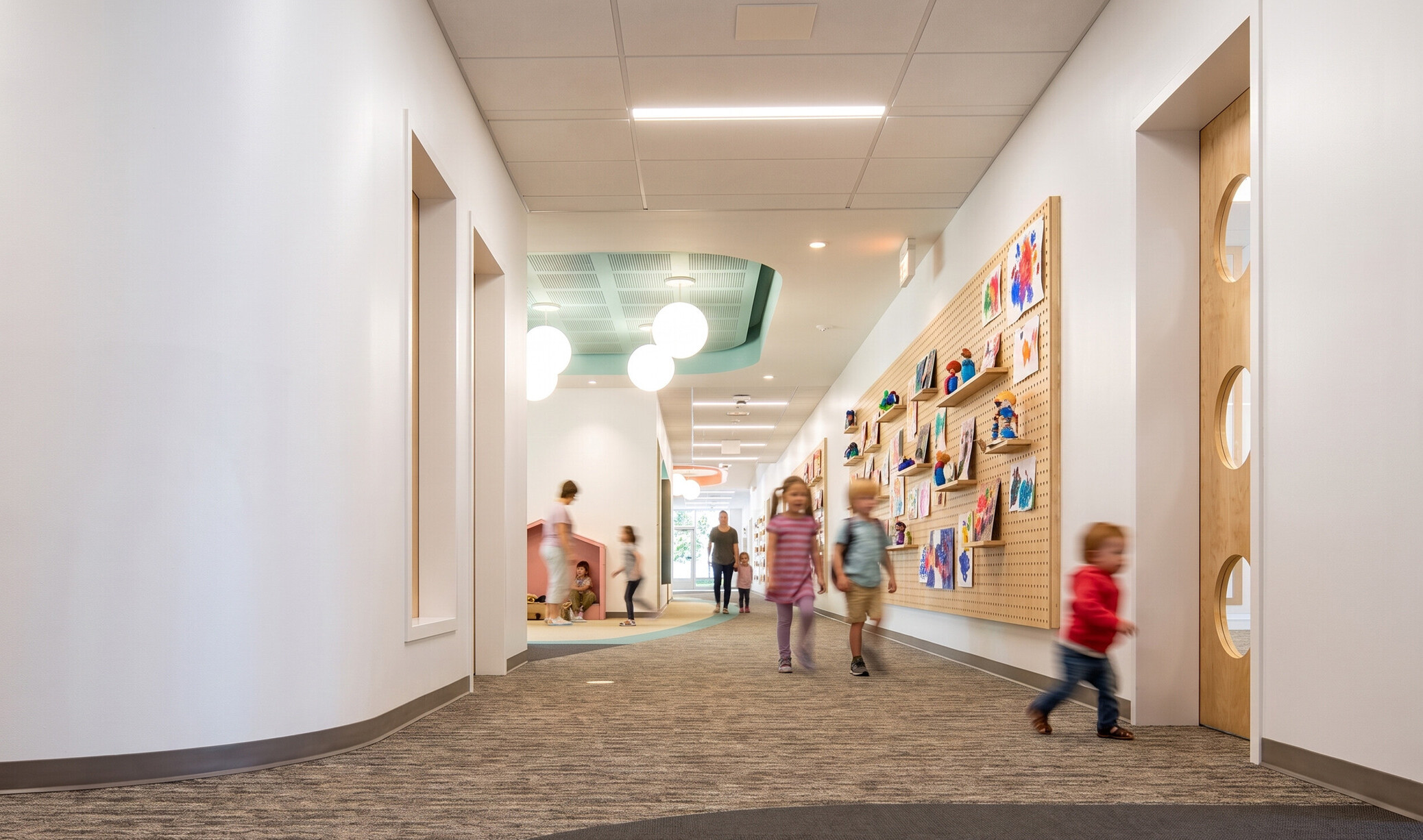 interior hallway of a school with children walking into a classroom with a colorful interactive art wall on the side of the door