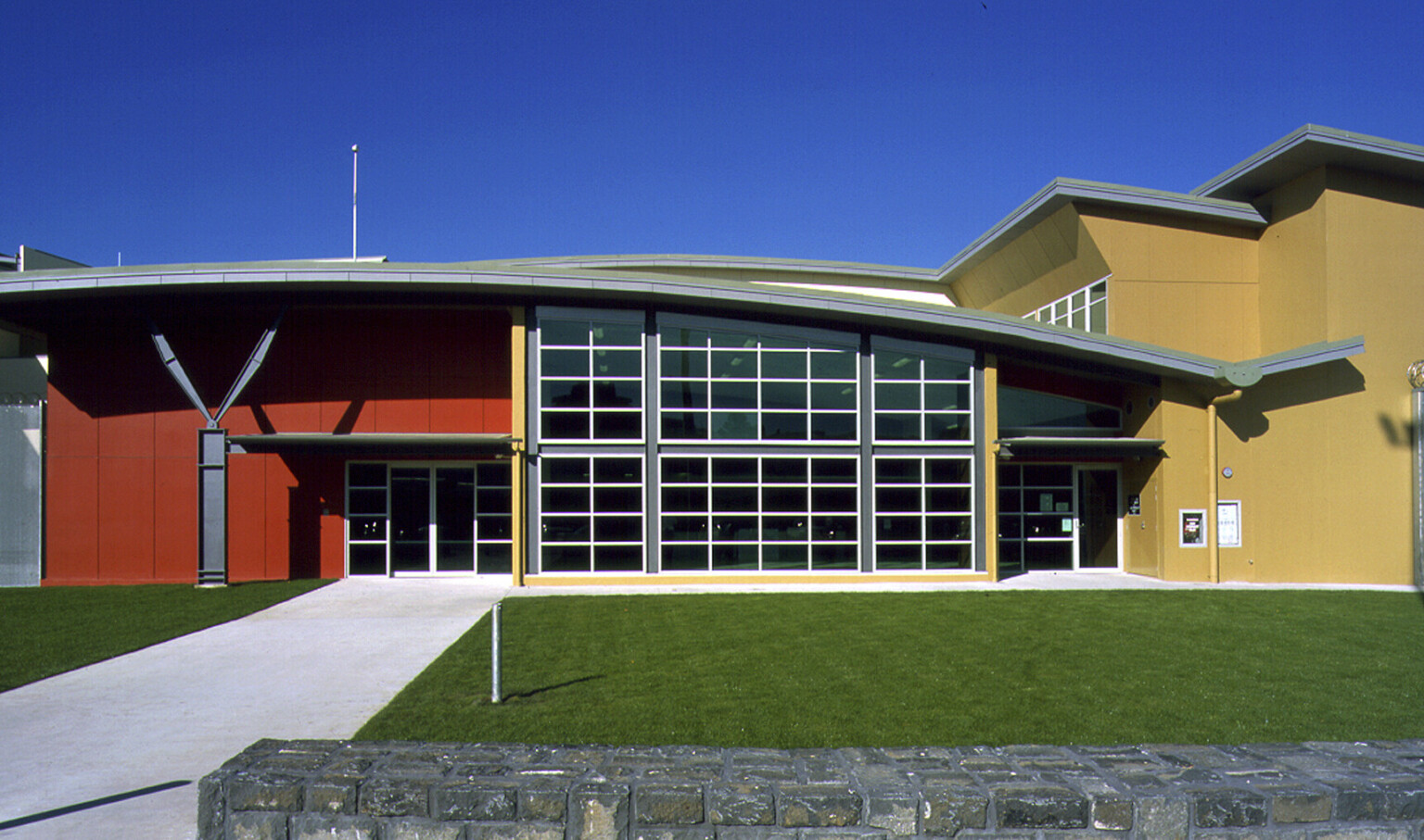 Closeup of entry. Double doors are to the left in a red painted portion, the rest of the building is painted a yellow brown