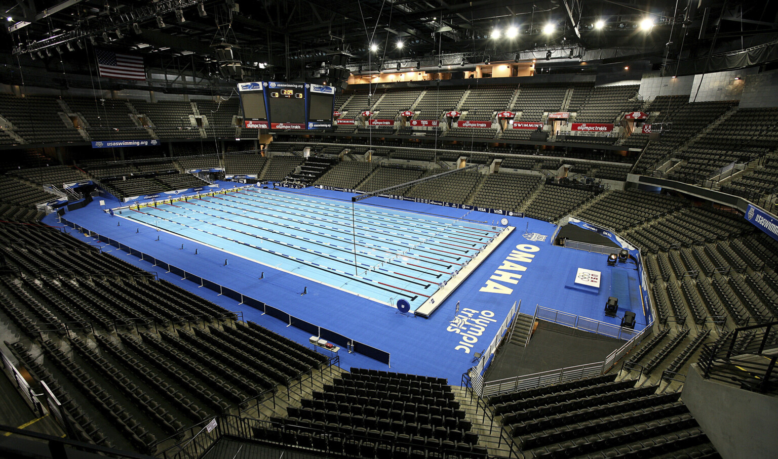A temporary Olympic sized swimming pool set up within the empty arena. Jumbotron above and poolside have Olympic trials signage