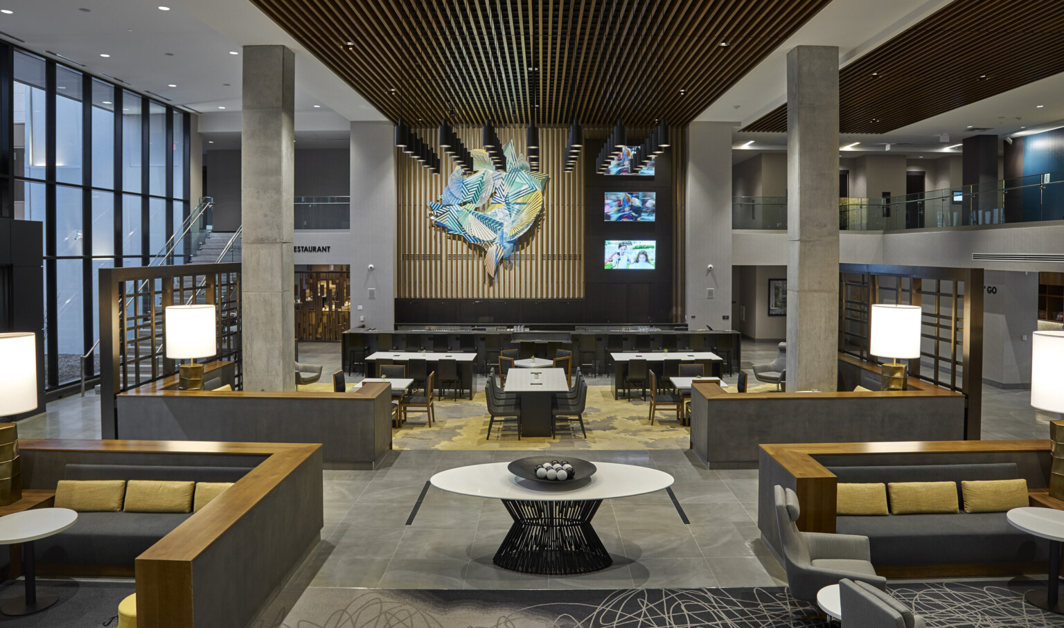 Mezzanine hallway in atrium with bar and tables at front of lower level. Stone pillars center and side 2nd floor walkways