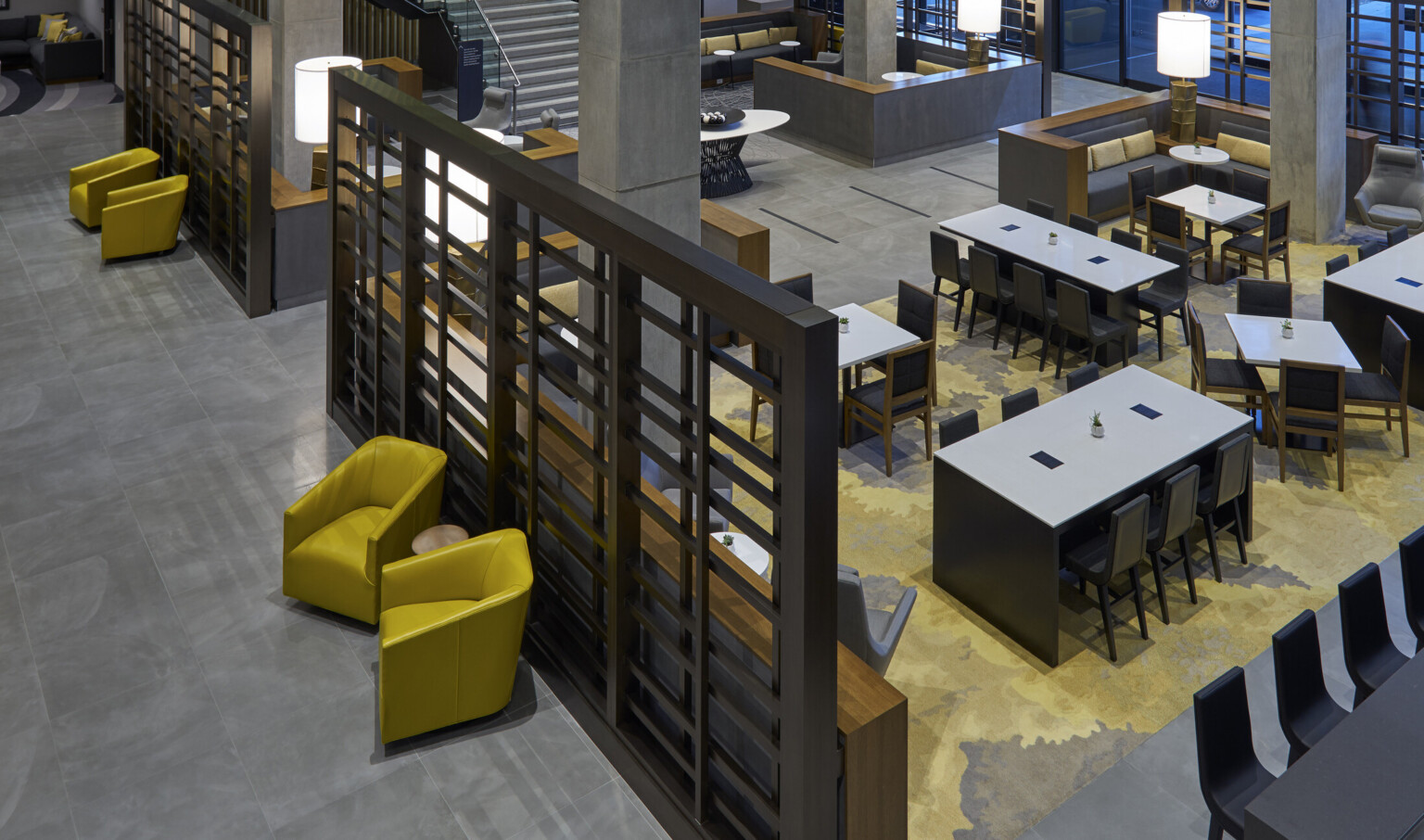 View from 2nd floor looking down on comfortable seating and dining areas. Black partitions with rectangular cutouts left