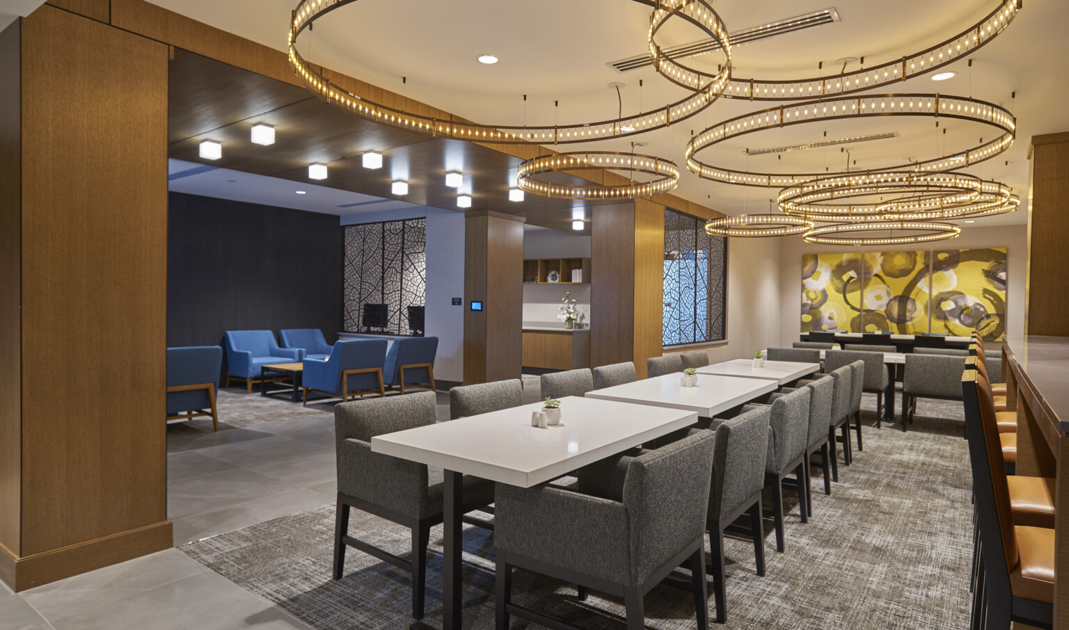 Long white tables with grey arm chairs with layer round chandeliers overhead. Adjoining grey room with blue chairs and table