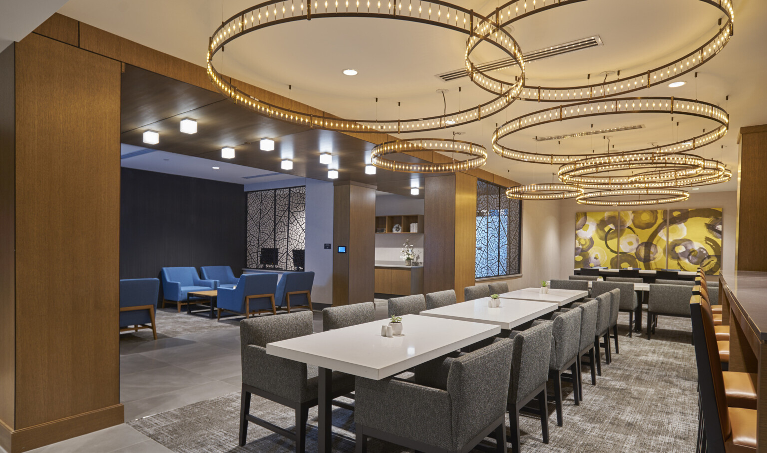 Long white tables with grey arm chairs with layer round chandeliers overhead. Adjoining grey room with blue chairs and table