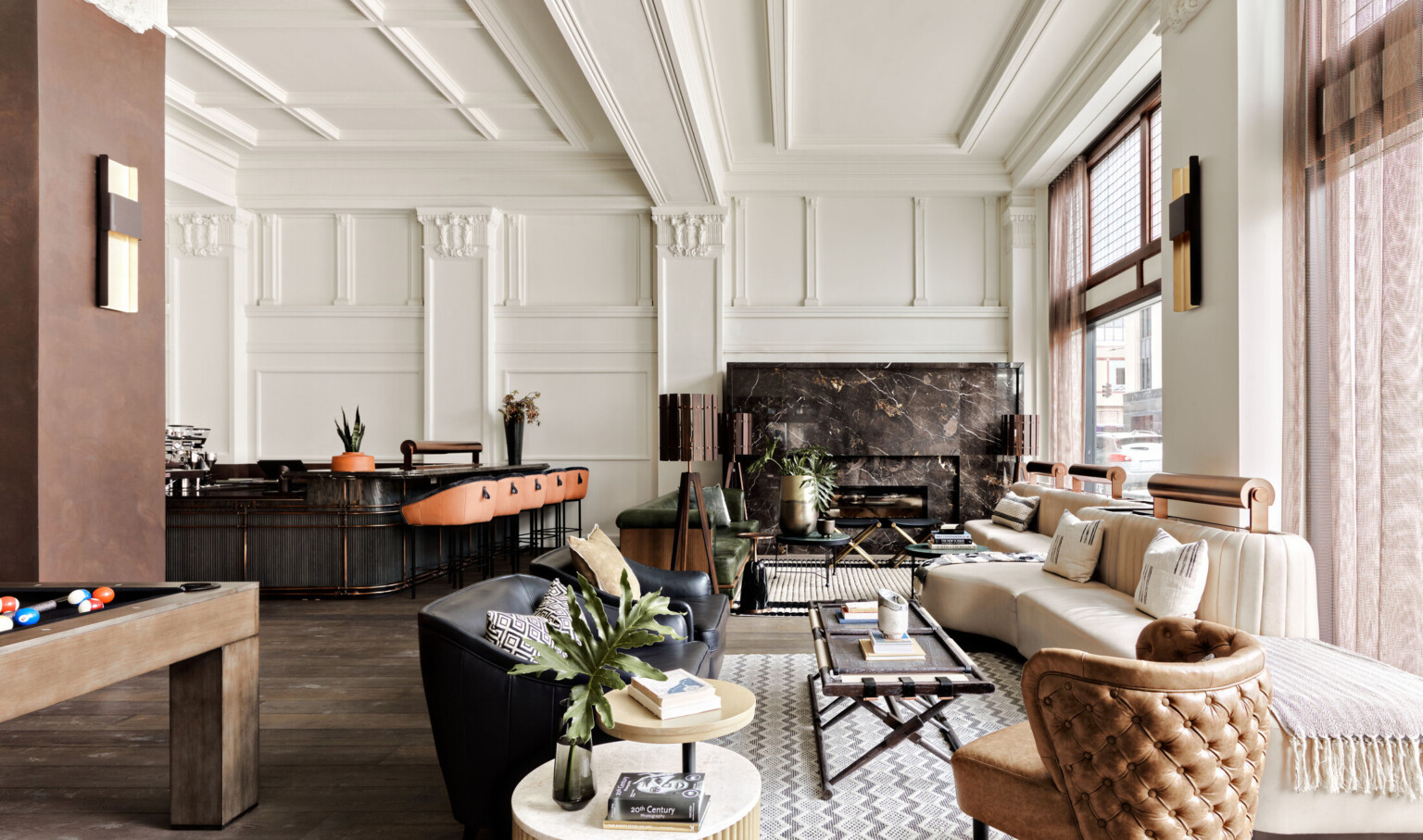 Seating area with arm chairs and cushioned bench along windows. Dark marbled fireplace on white wall with pillars and molding