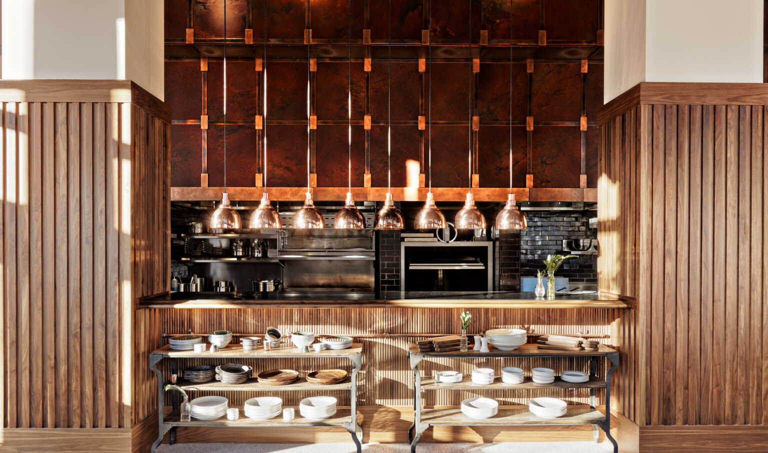 Wood walls and counter with cutout to exposed dark brick kitchen. Wood and metal shelves under counter, appliances behind