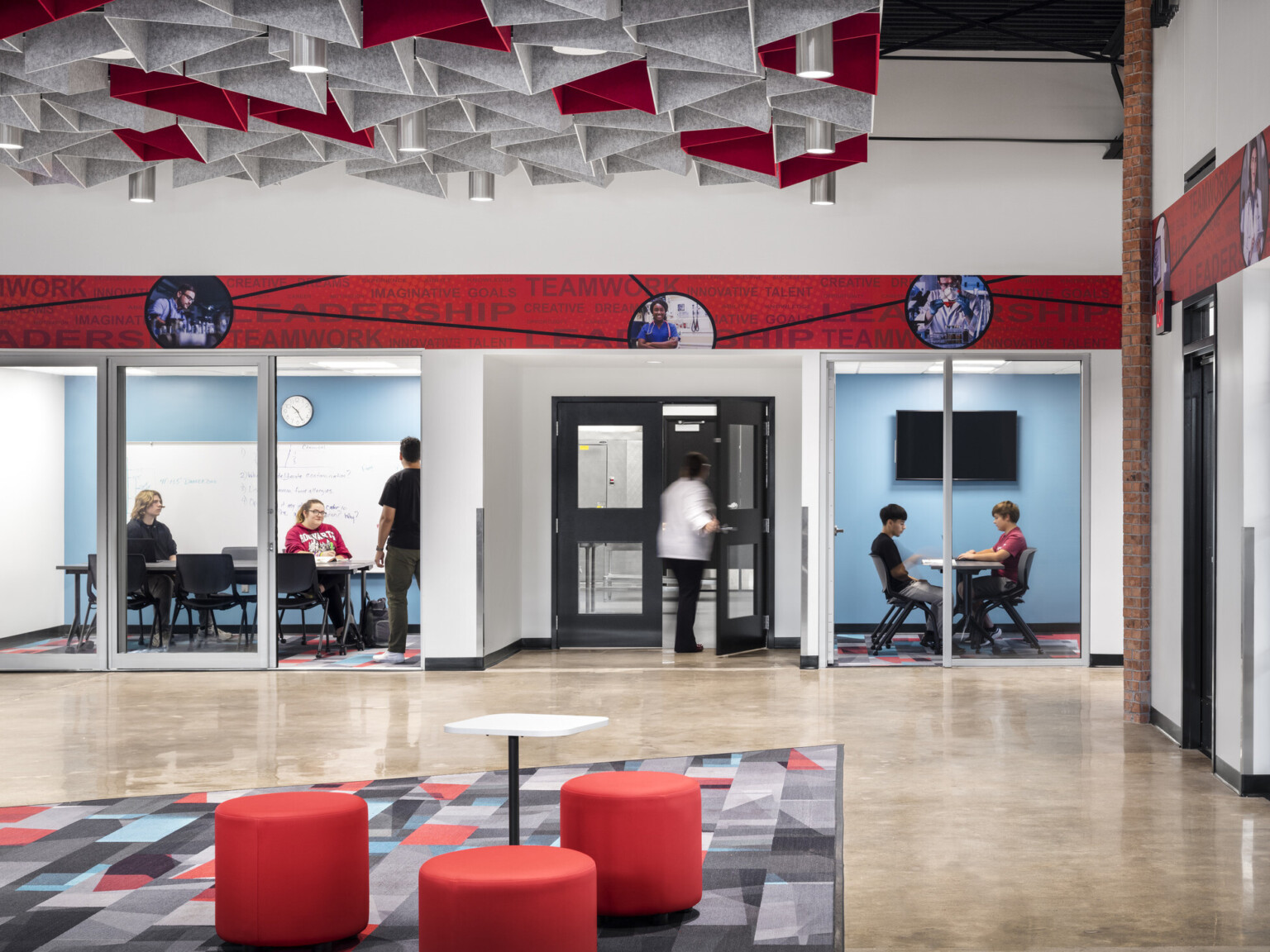 Ottumwa Career Campus interior seating area with grey and red baffles above mixed seating space, glass garage doors, glass-walled conference rooms provide quiet and privacy