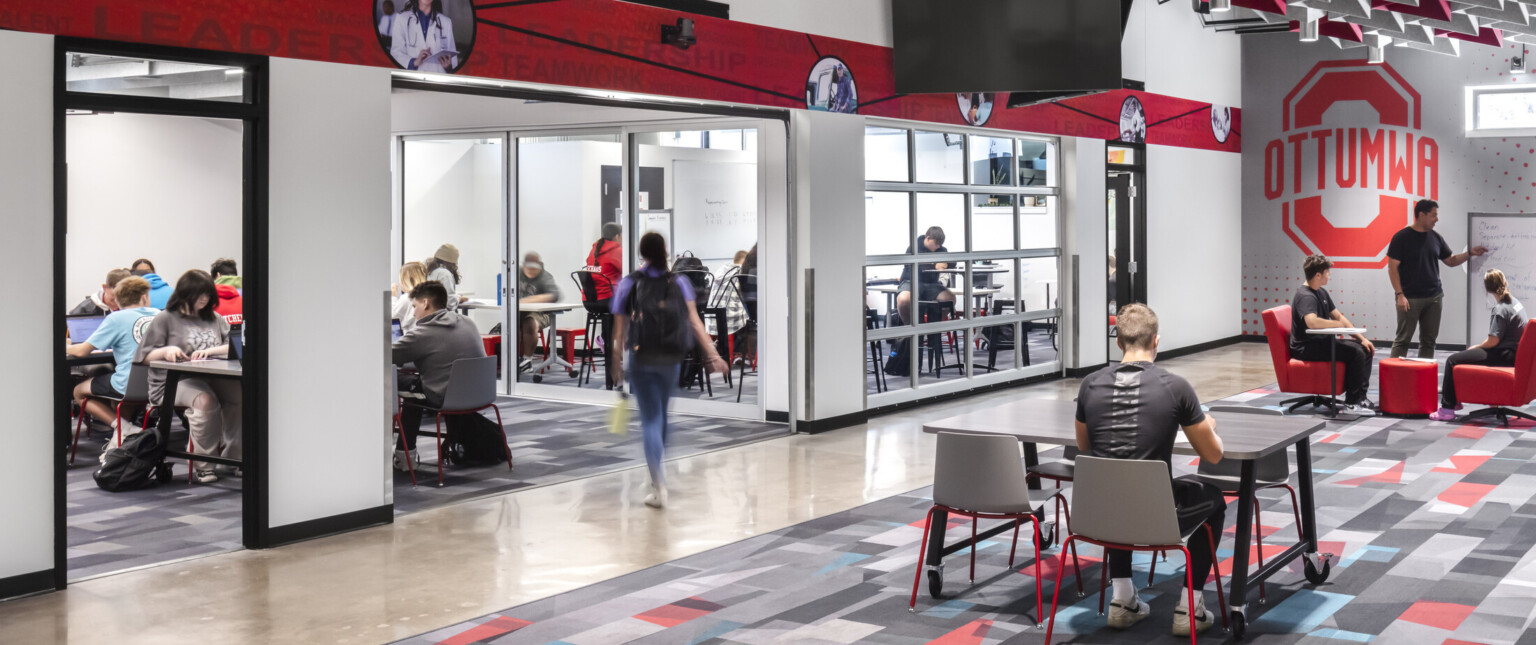 Ottumwa Career Campus interior seating area with grey and red baffles above mixed seating space, glass garage doors