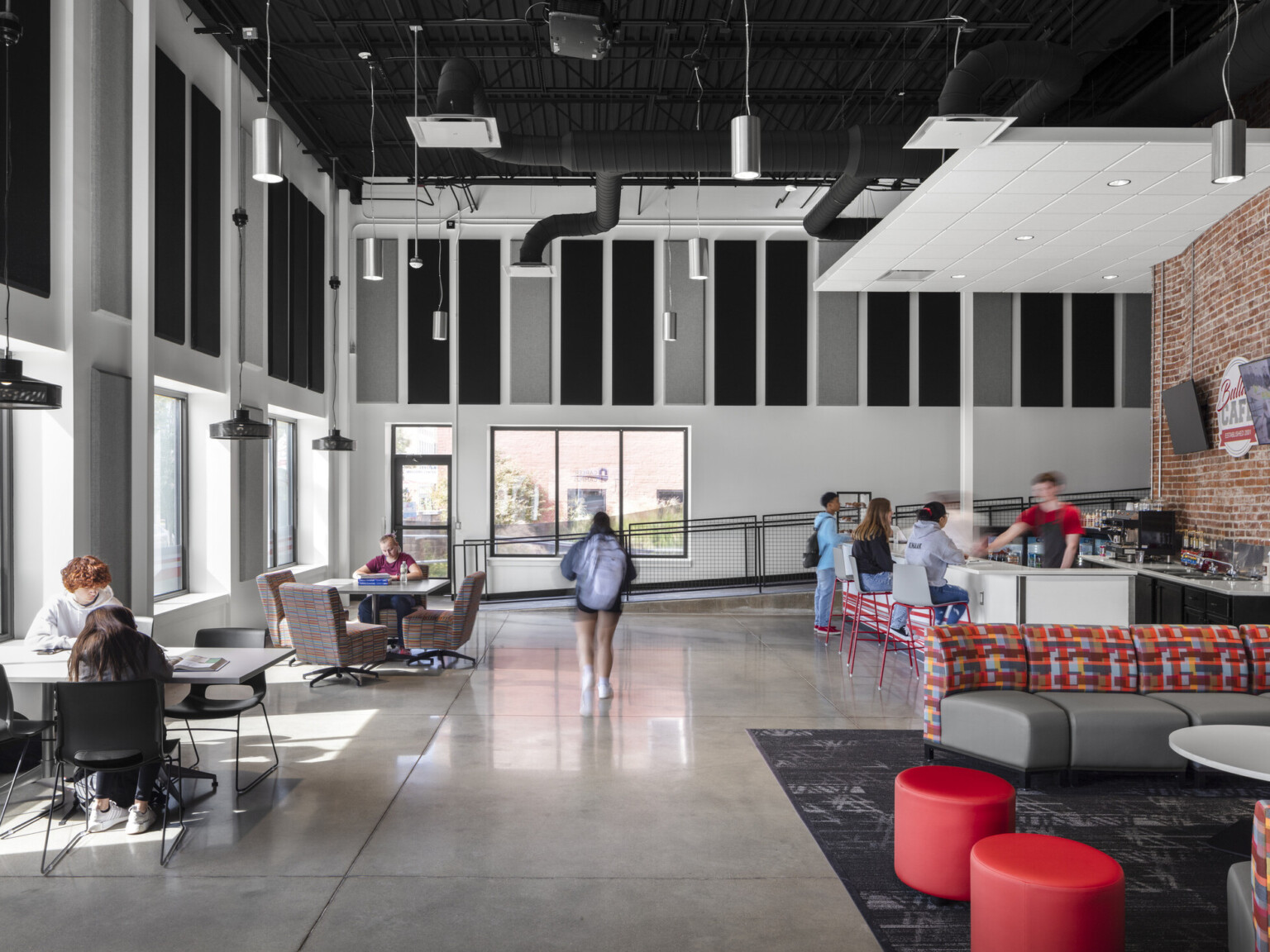 Ottumwa Career Campus interior seating area with grey and red baffles above mixed seating space, glass garage doors, large windows provide natural light