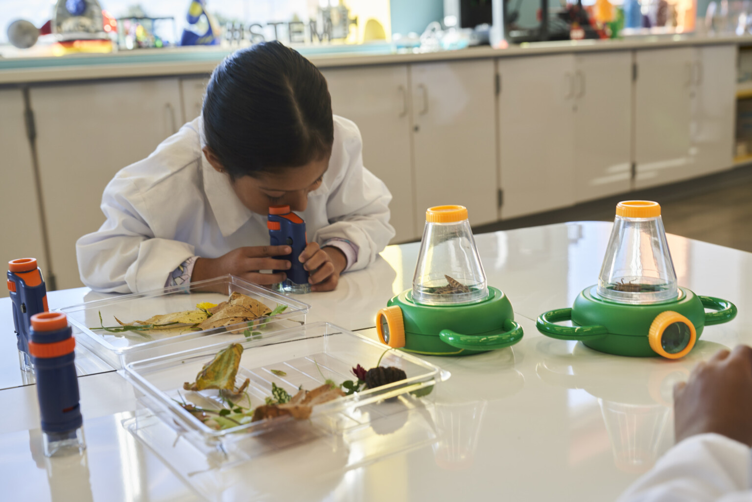 Young girl in lab coat looking in microscope in a science lab.