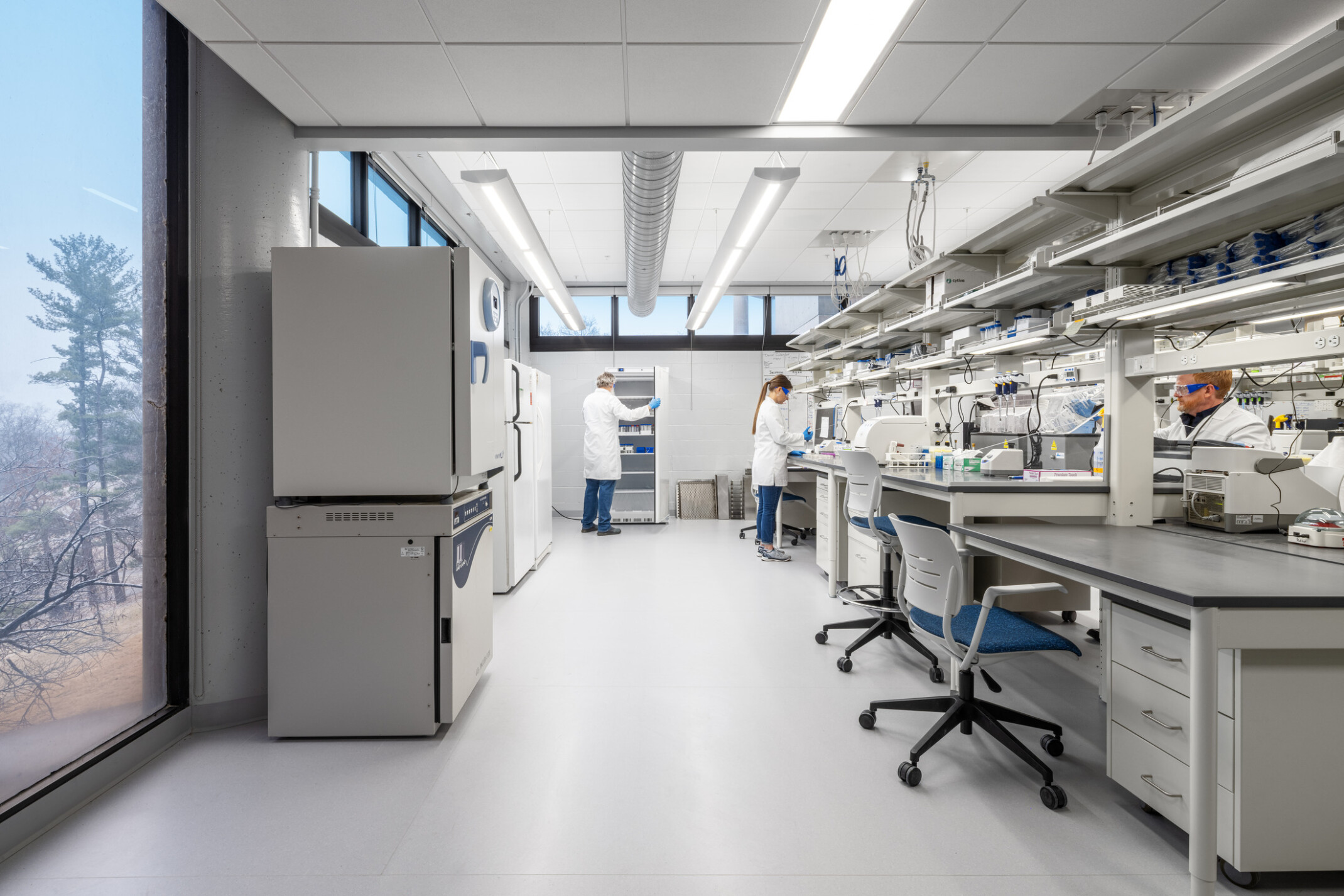 modern science lab with people in white coats attending to the counter; beakers, fridges, medical equipment throughout