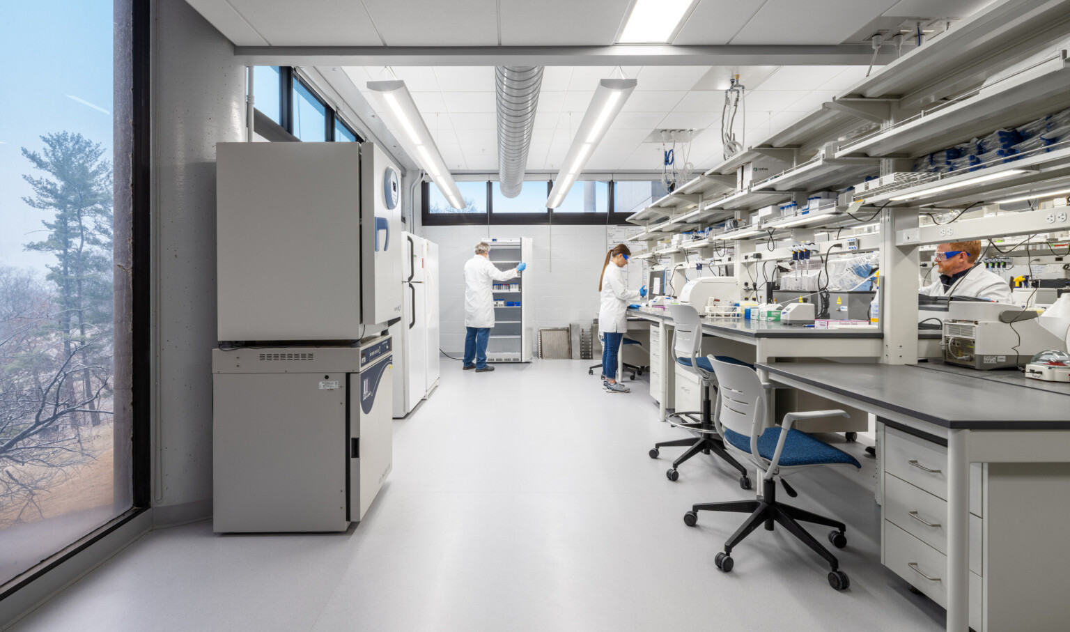 modern science lab with people in white coats attending to the counter; beakers, fridges, medical equipment throughout