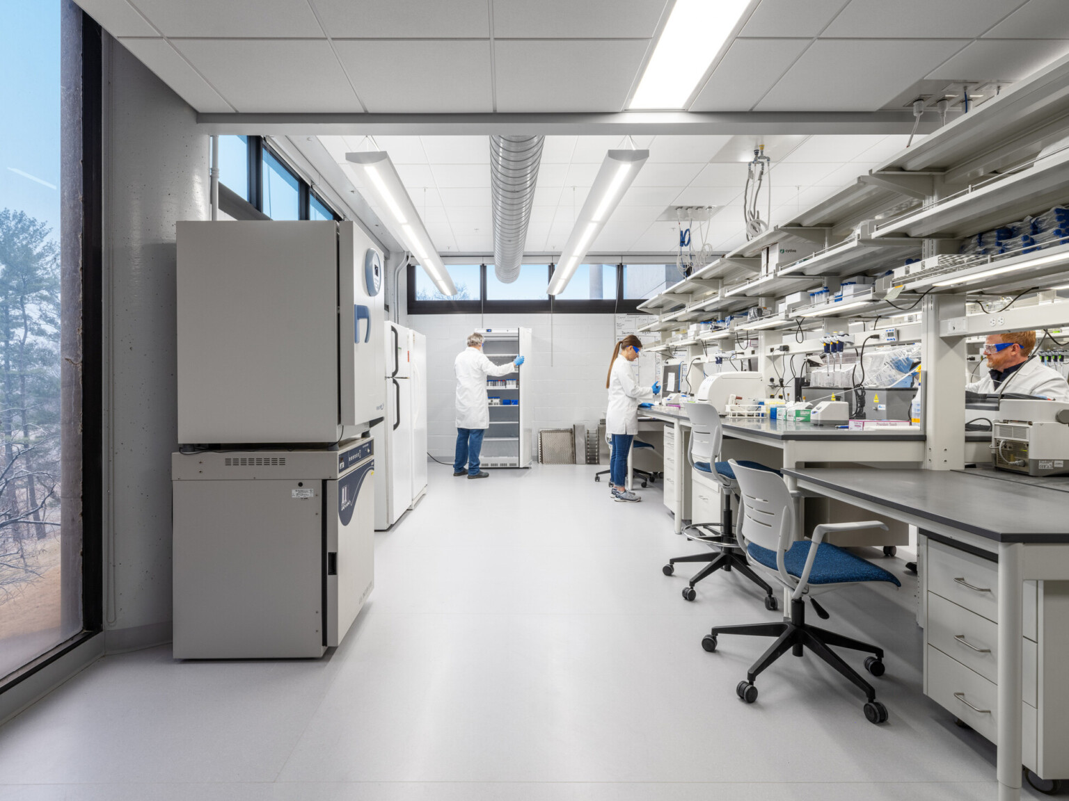 modern science lab with people in white coats attending to the counter; beakers, fridges, medical equipment throughout modern science lab with people in white coats attending to the counter; beakers, fridges, medical equipment throughout
