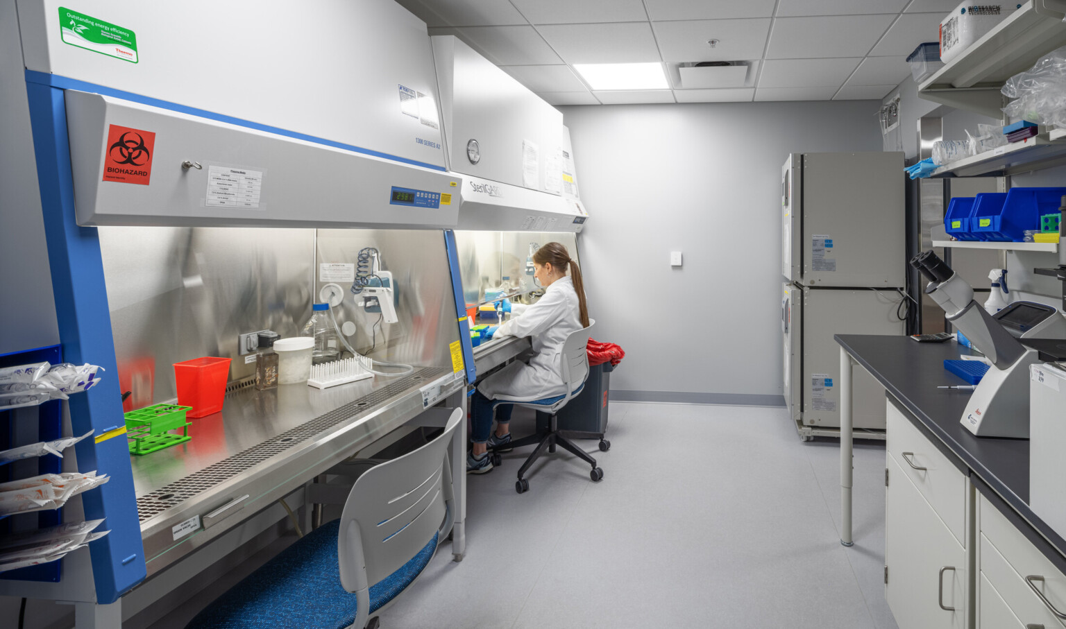 modern science lab with a woman in white coat attending to the counter; beakers, fridges, medical equipment throughout